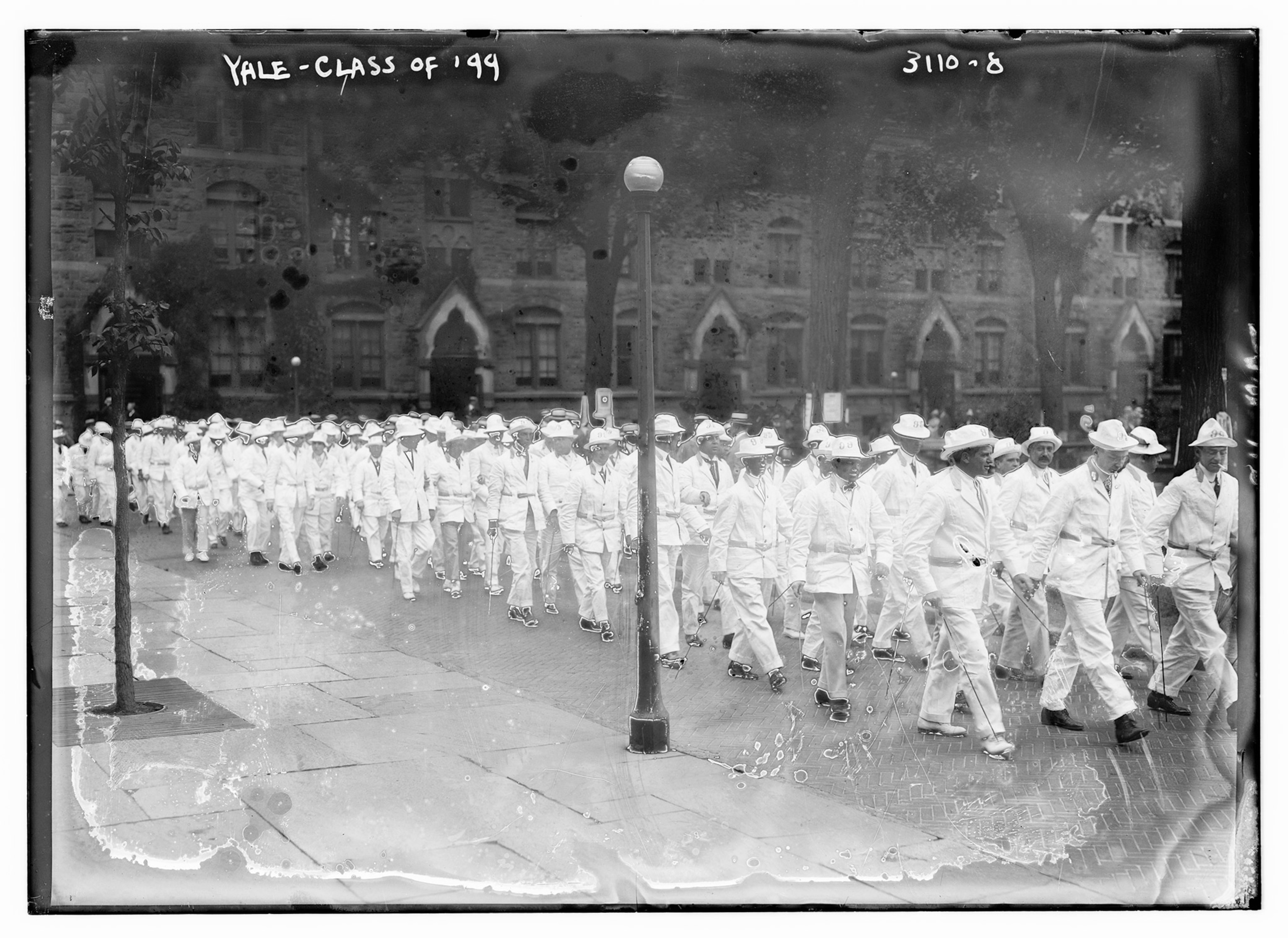 A black and white photograph of men in a procession wearing white suits and top hats.