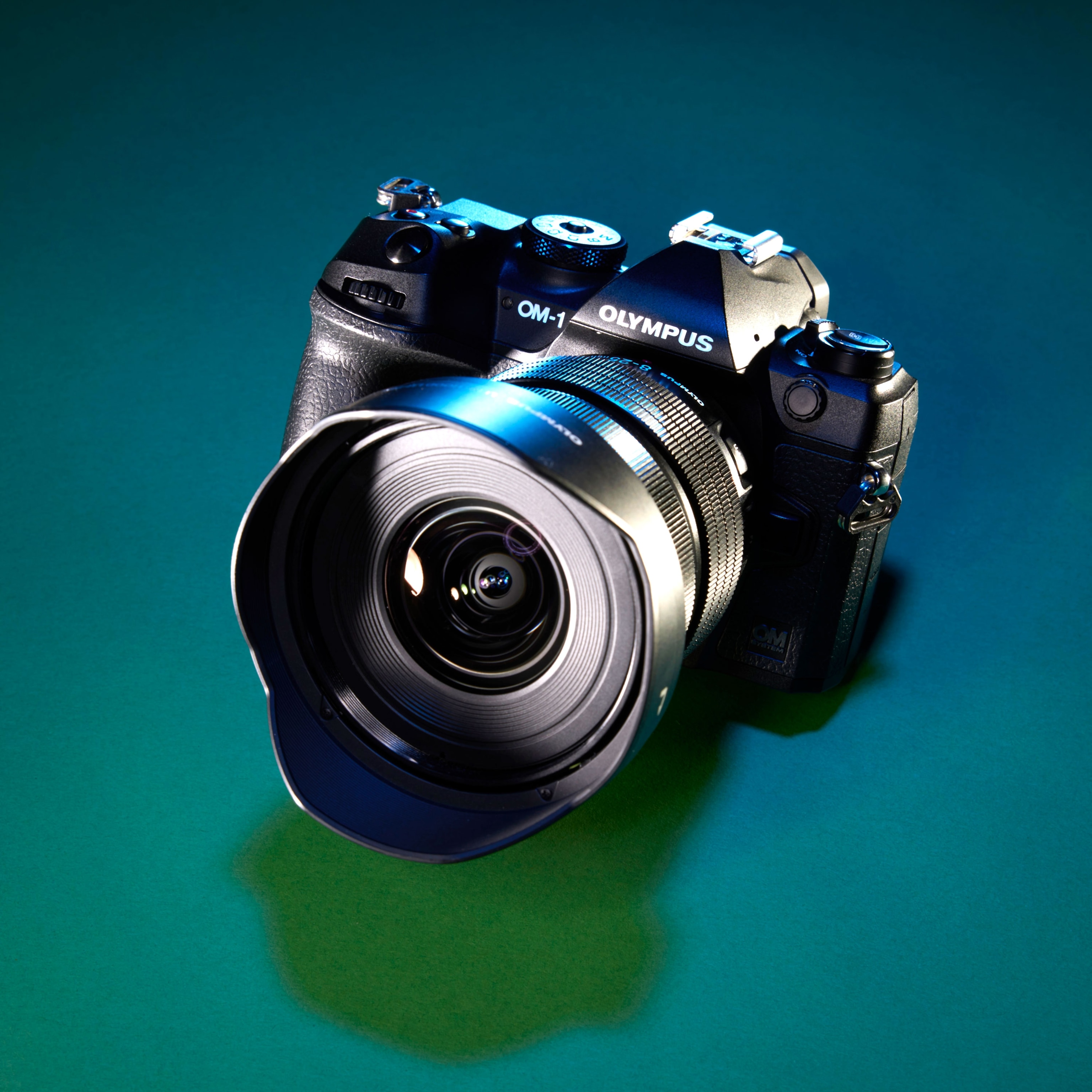 Studio photograph of a OM Systems OM-1 camera against a teal gradient background