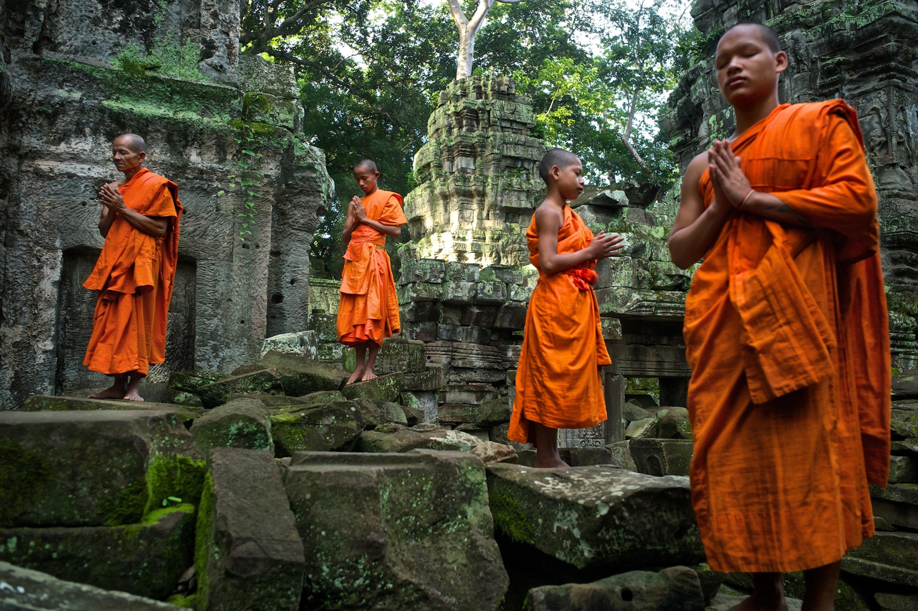 Picture of four monks in orange robes by ruins ancient.