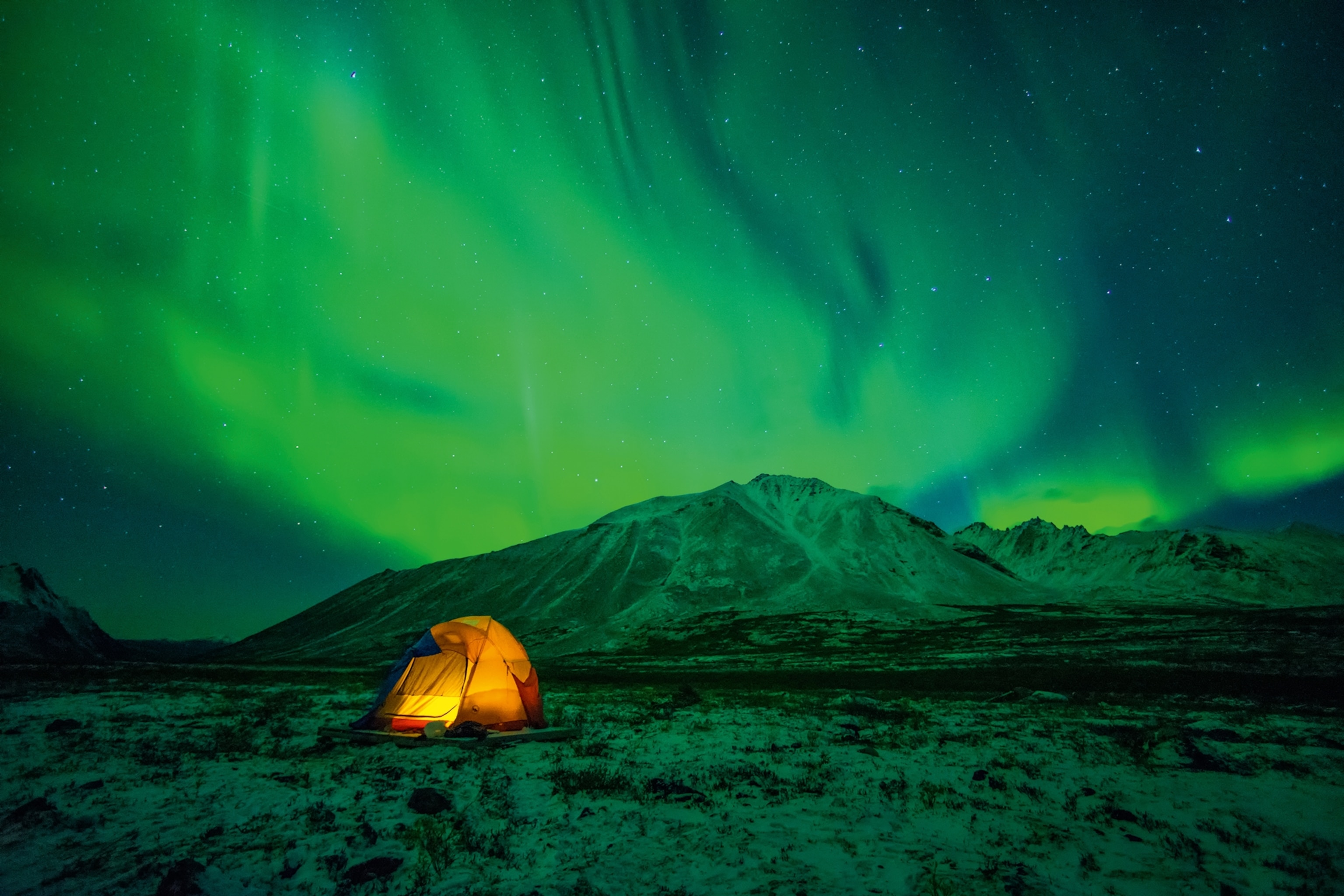 A tent camping under the Aurora Borealis, mountain range in the background.