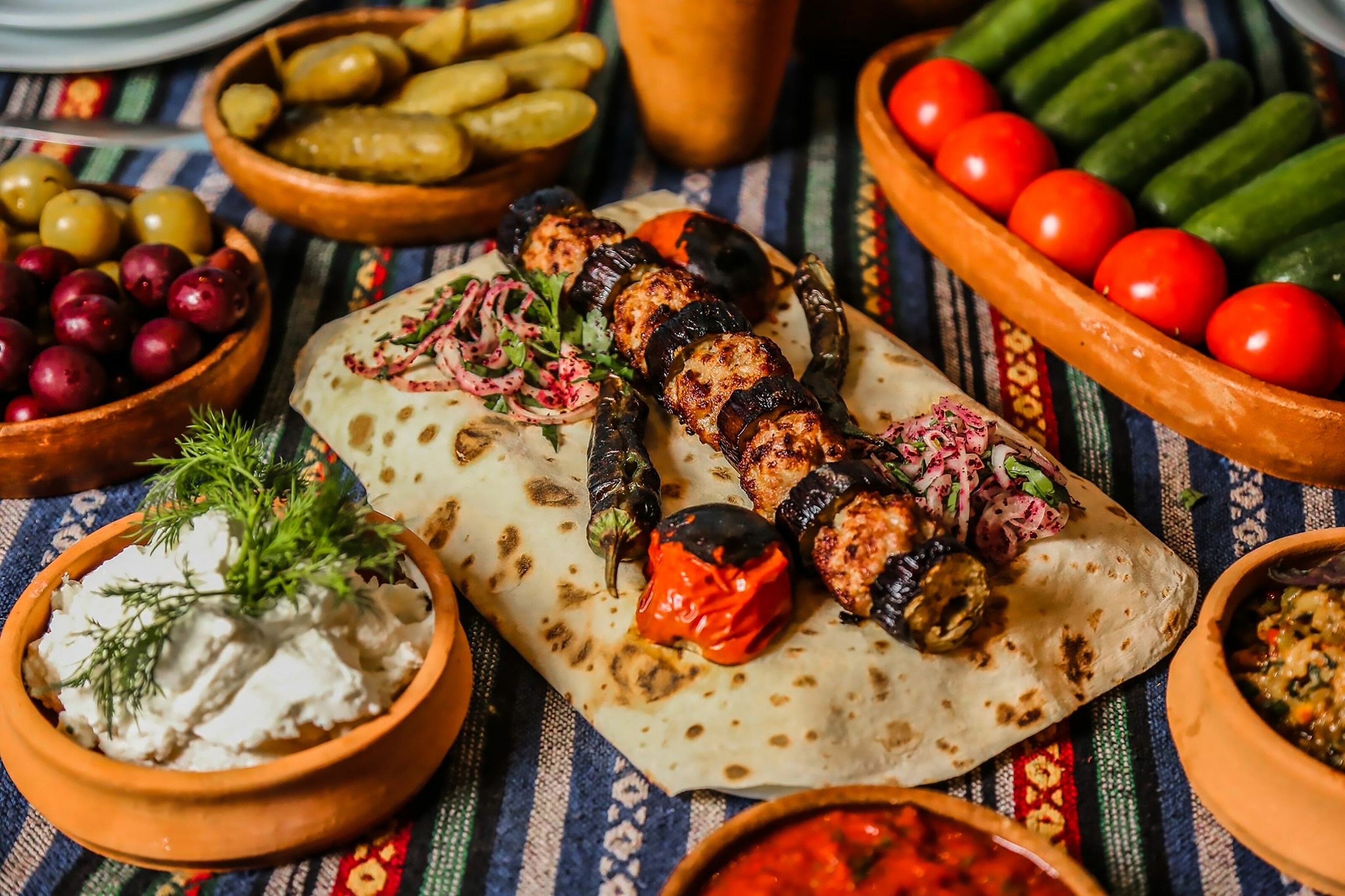 Kebabs laid out alongside dishes of fruits, dips and pickles.