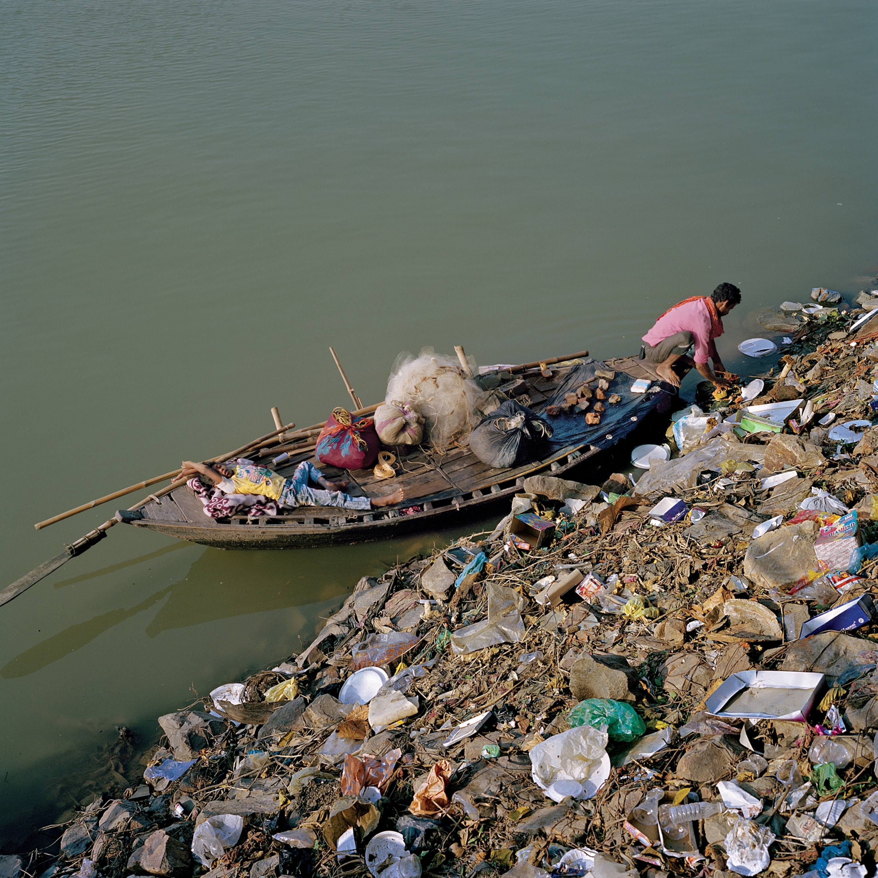 Picture of boy resting on fishing boat while his father is landing on trash dumping site.