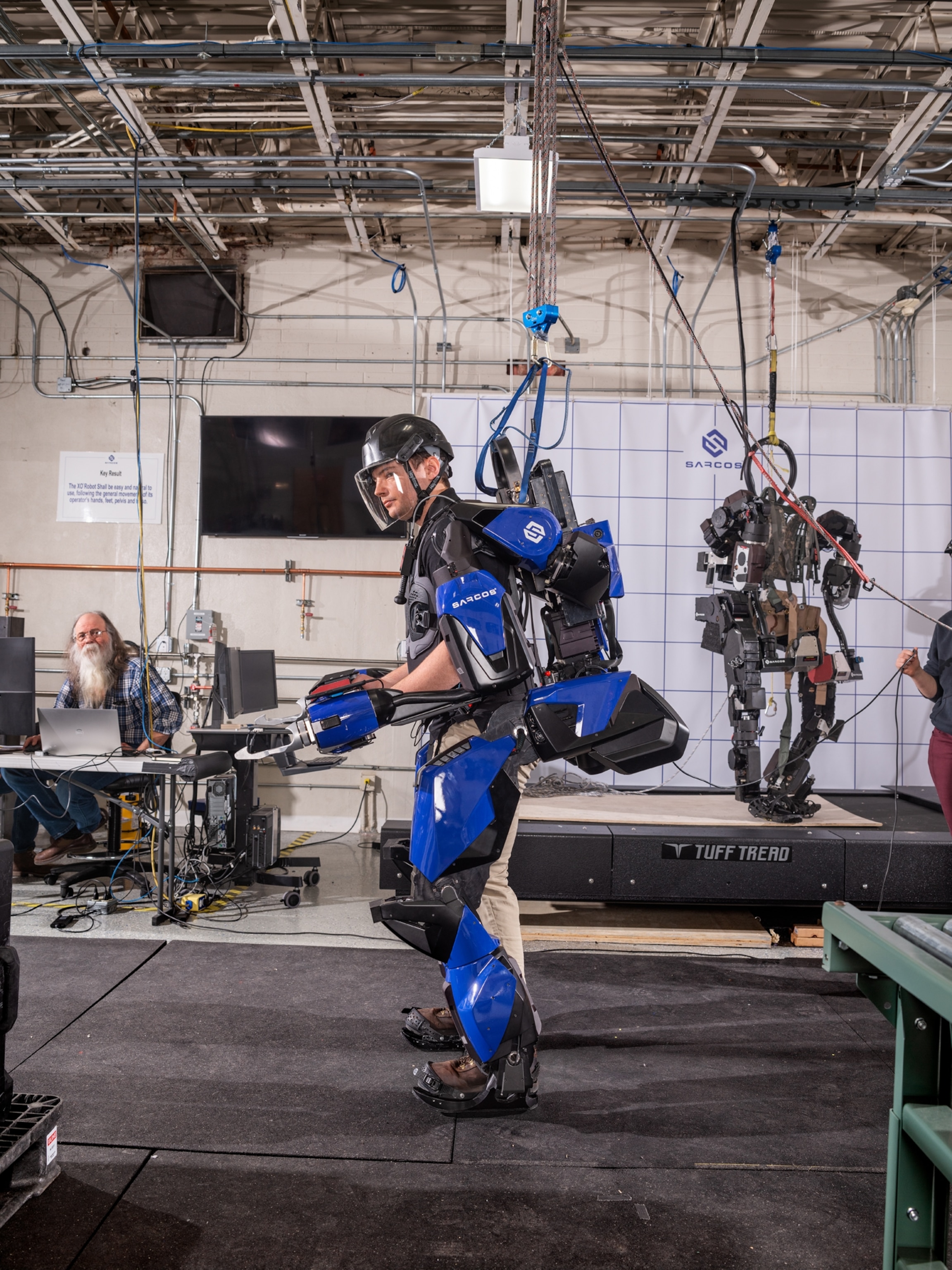 man in helmet and blue armor holding a power tool.