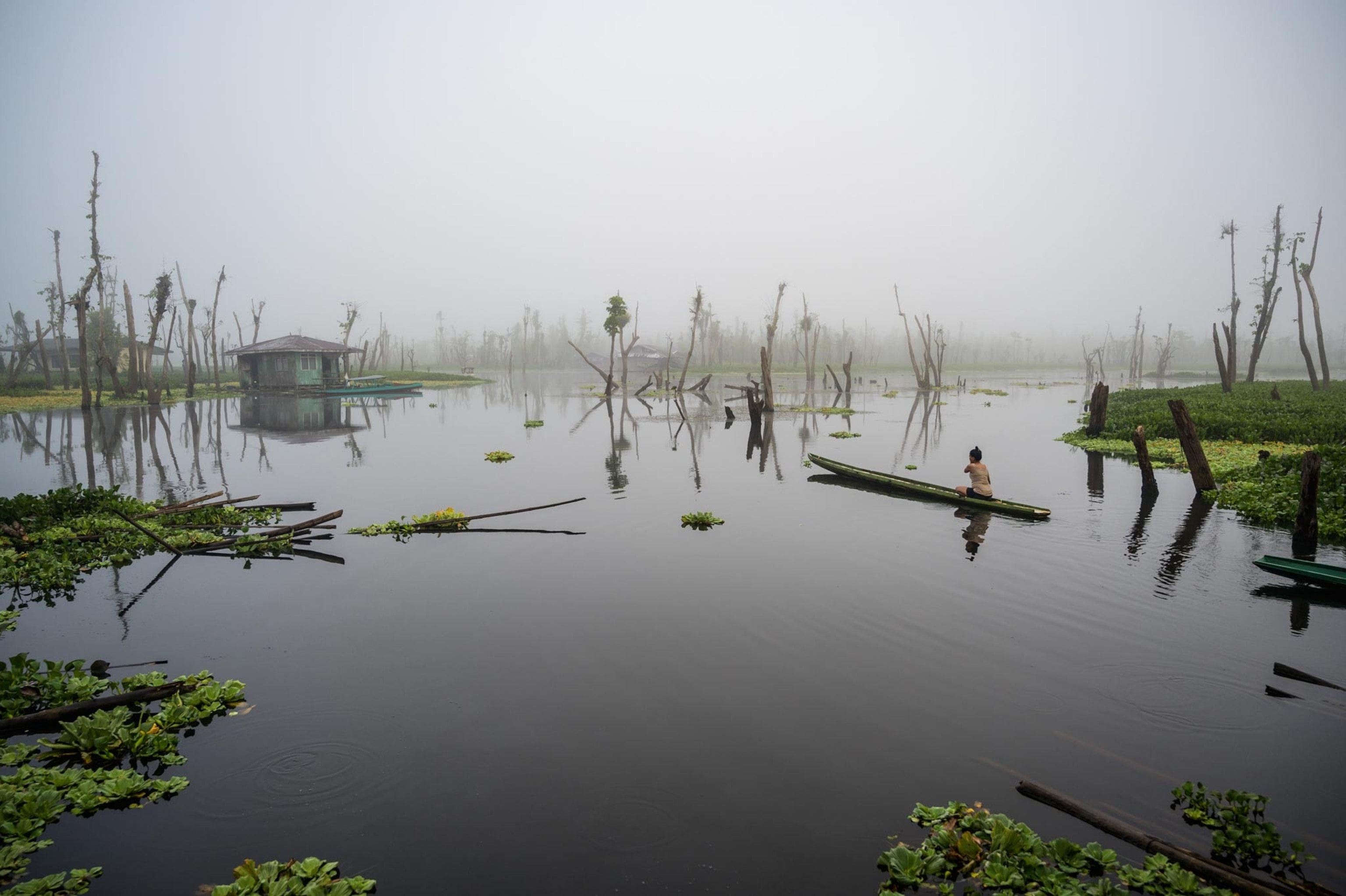 woman on a canoe in a body of water moving away from the camera and towards fog