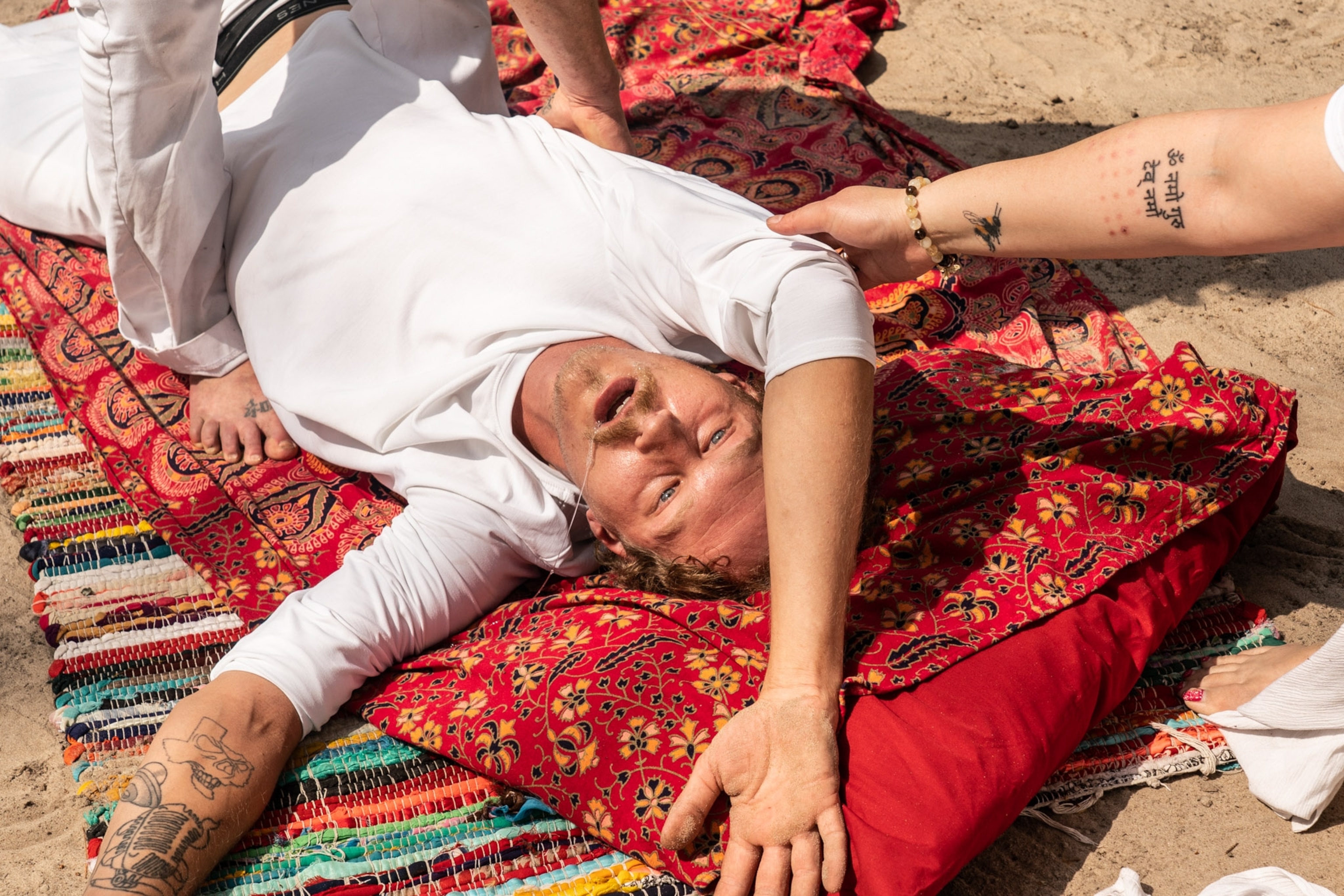A man lays with druel coming out of his mouth he stares off into the distance as people help him.