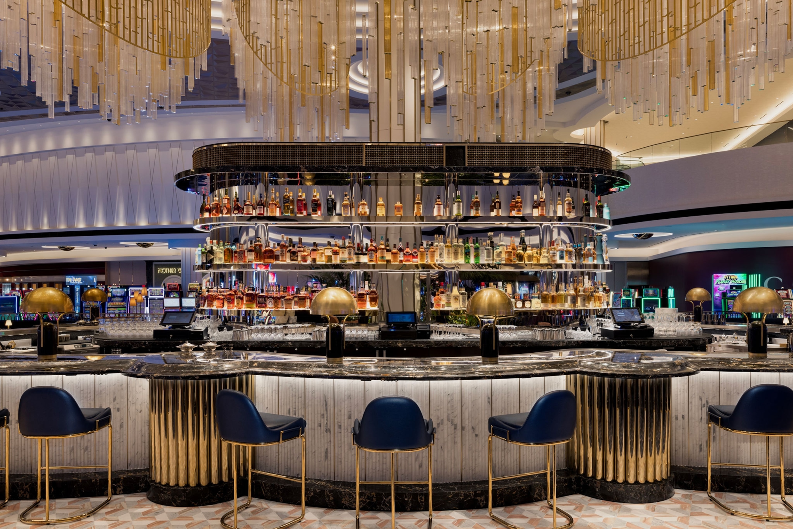 A glamorous bar with lights, gold and slot machines in the back.