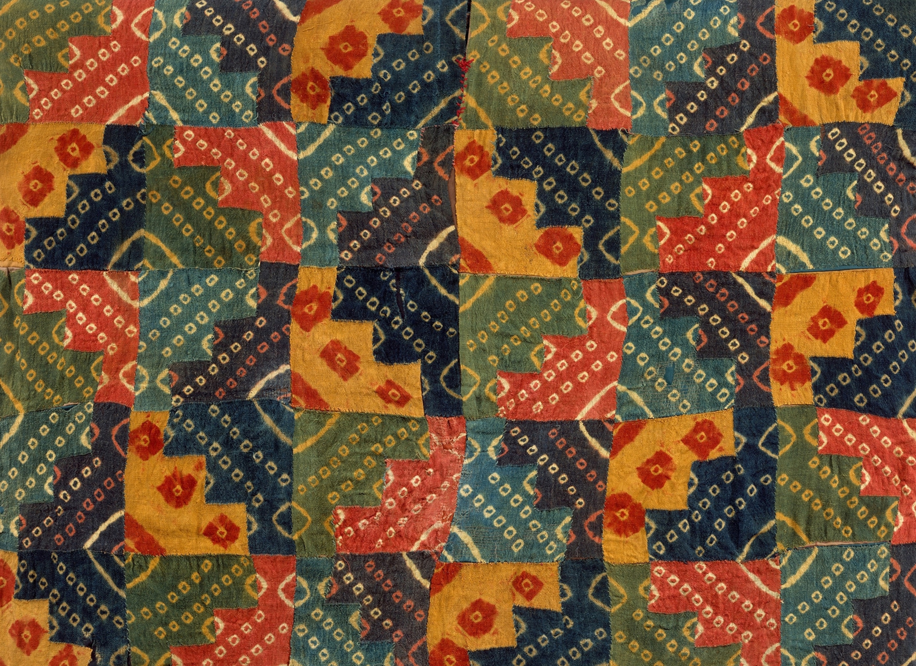 A patchwork tunic of Peru made of patches of cloth dyes in colors of blue, yellow, green, and red.