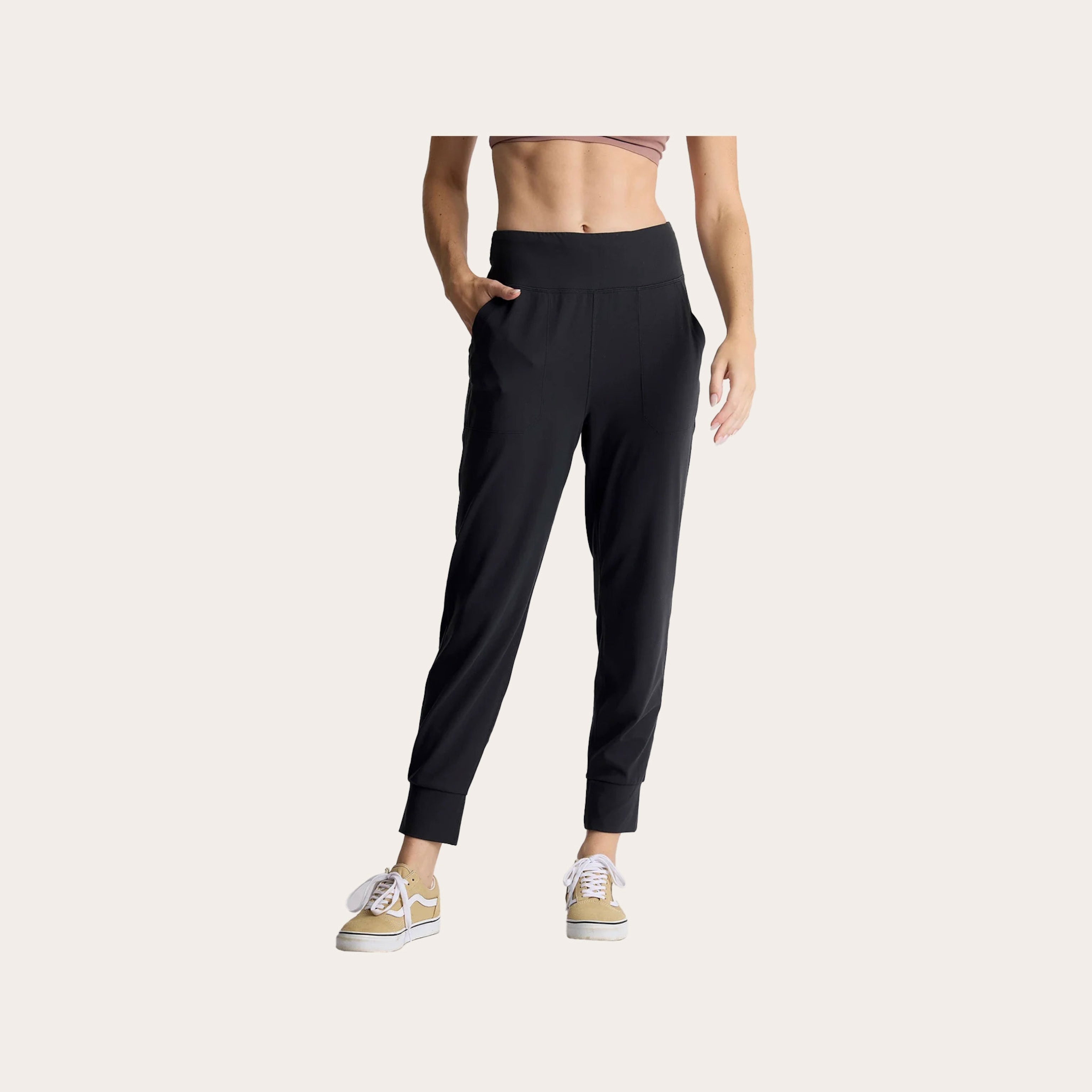 Woman wearing black jogger pants in front of a tan background.