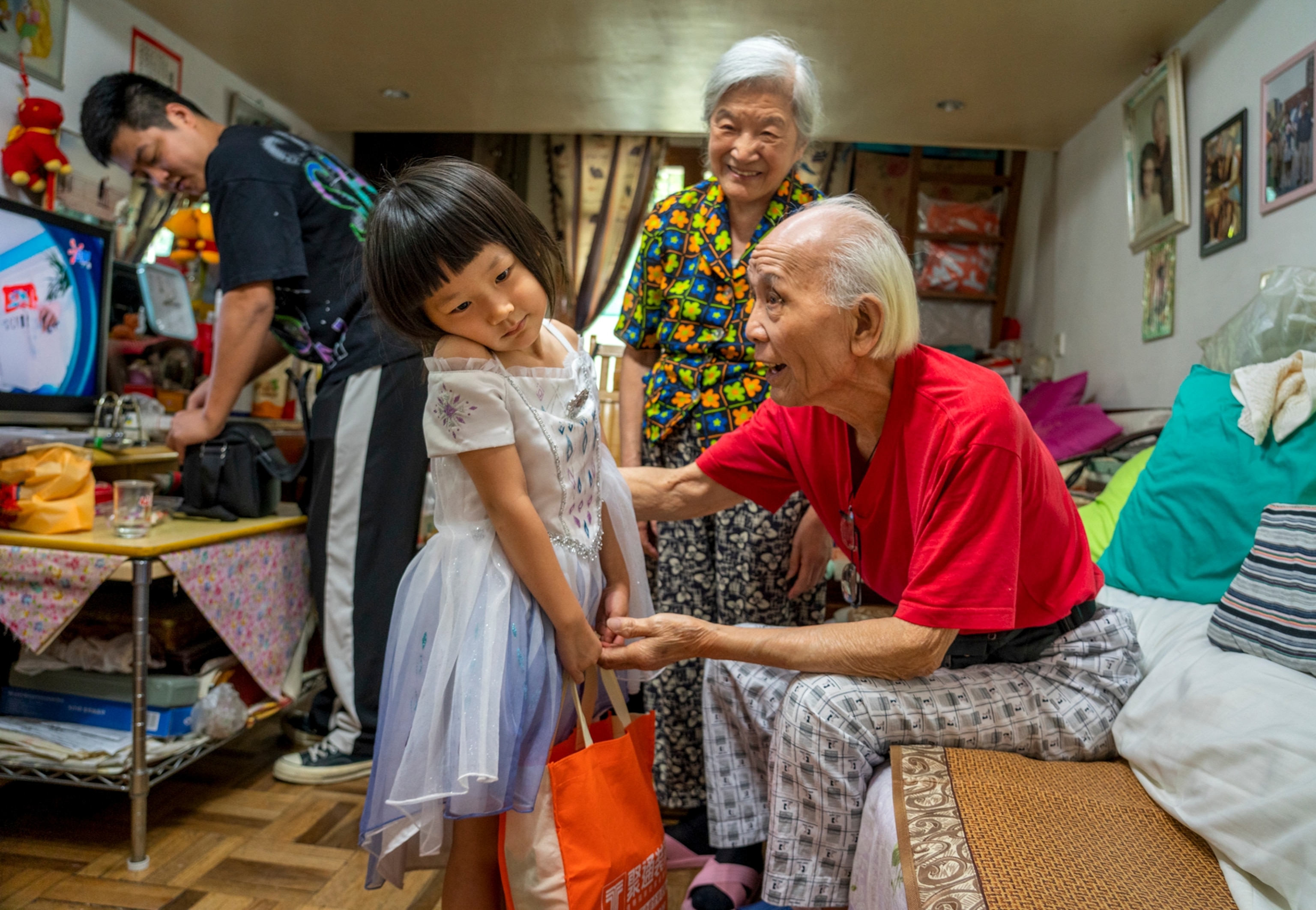 Picture of old man with grey hair in red shirt talking to the little girl in white dress.