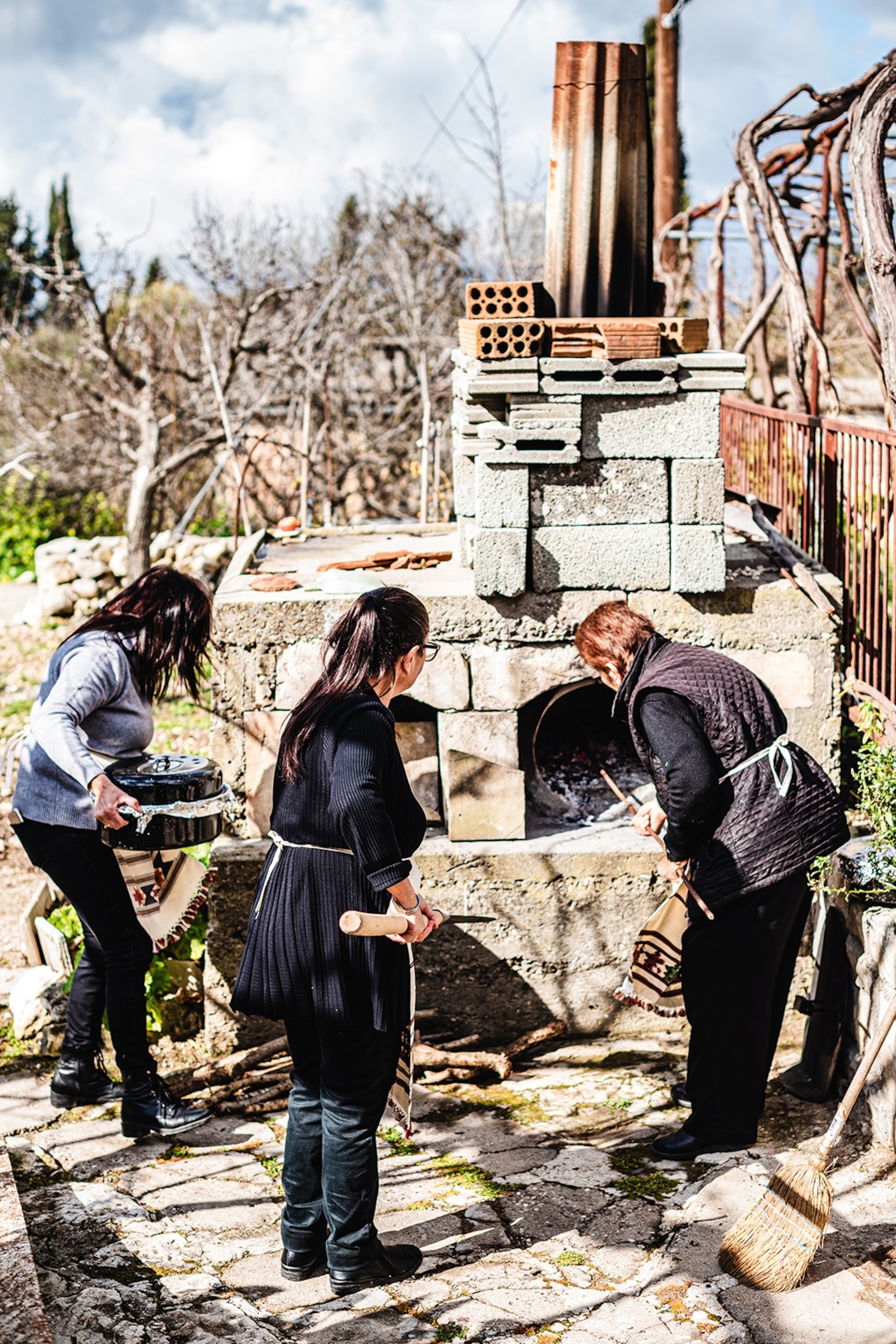 Three women crowd around a brick clay oven in a garden