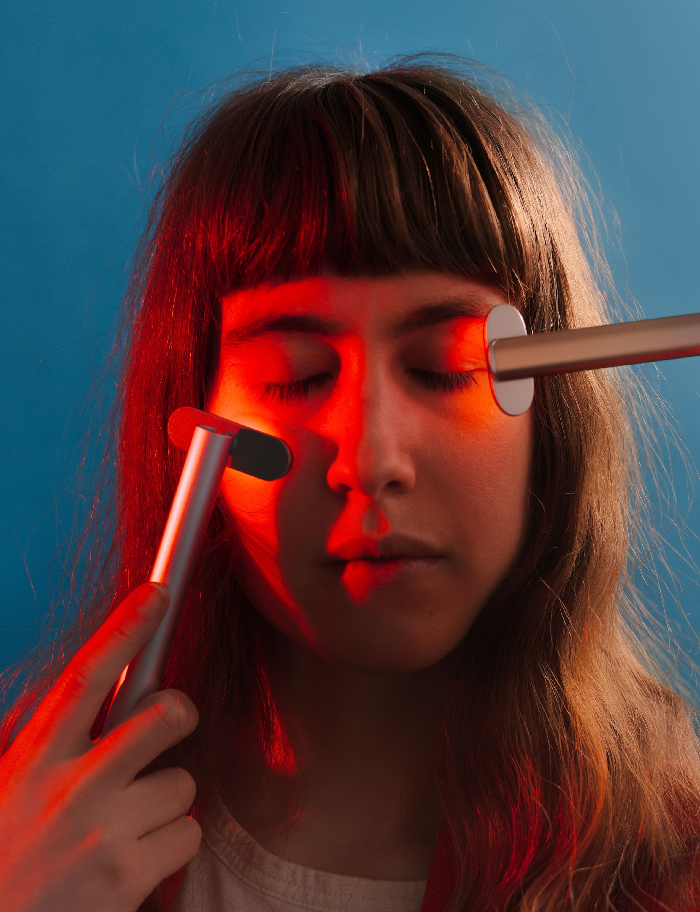 A model poses for a portrait with two handheld LED wands designed for consumer use in a studio against a blue background