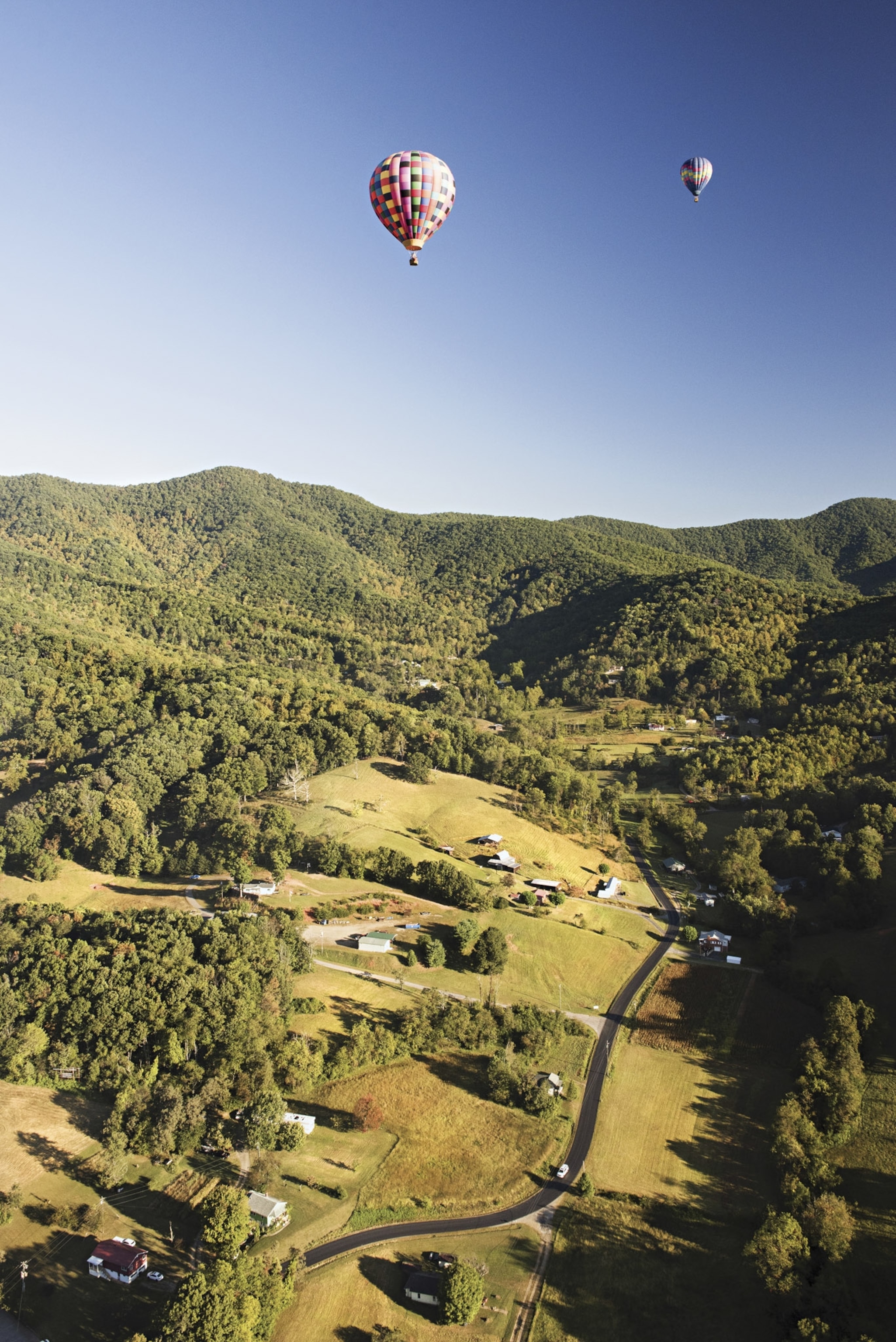 Lush green hills and hot air balloons in a clear blue sky.
