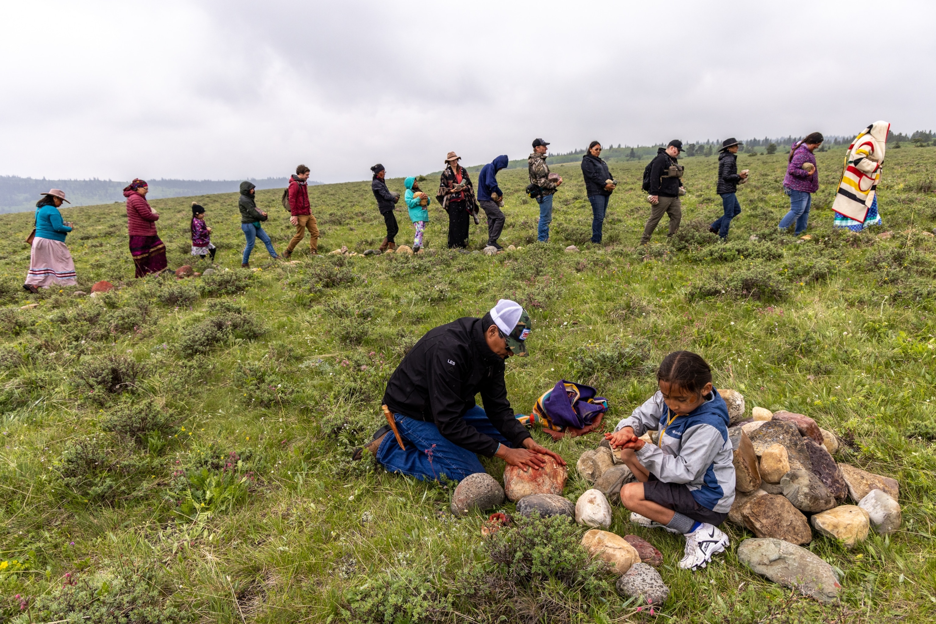 A Blackfoot elder shows Ashton Falcon how to paint rocks for the medicine wheel that is being constructed at the site where the Blackfeet buffalo will be released near Chief Mountain.