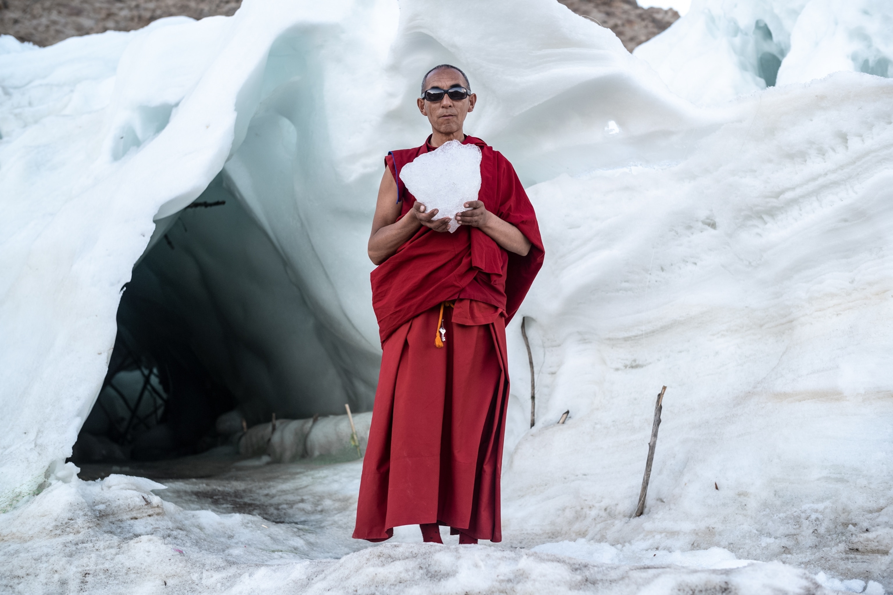 Buddhist monk in red robe holding chunk of ice.