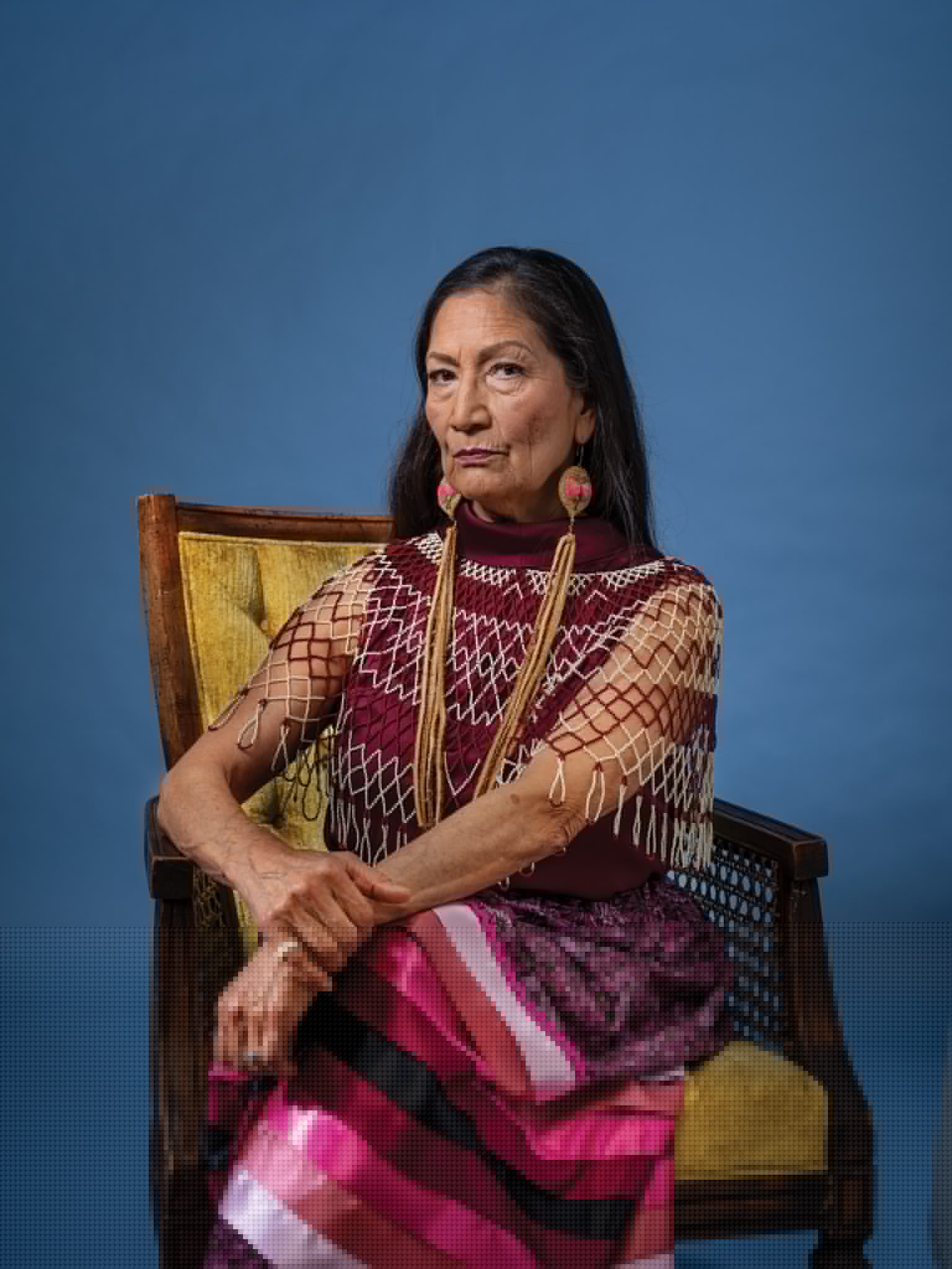 Women with long dark hair and traditional jewelry sitting in armchair and looking into the camera.