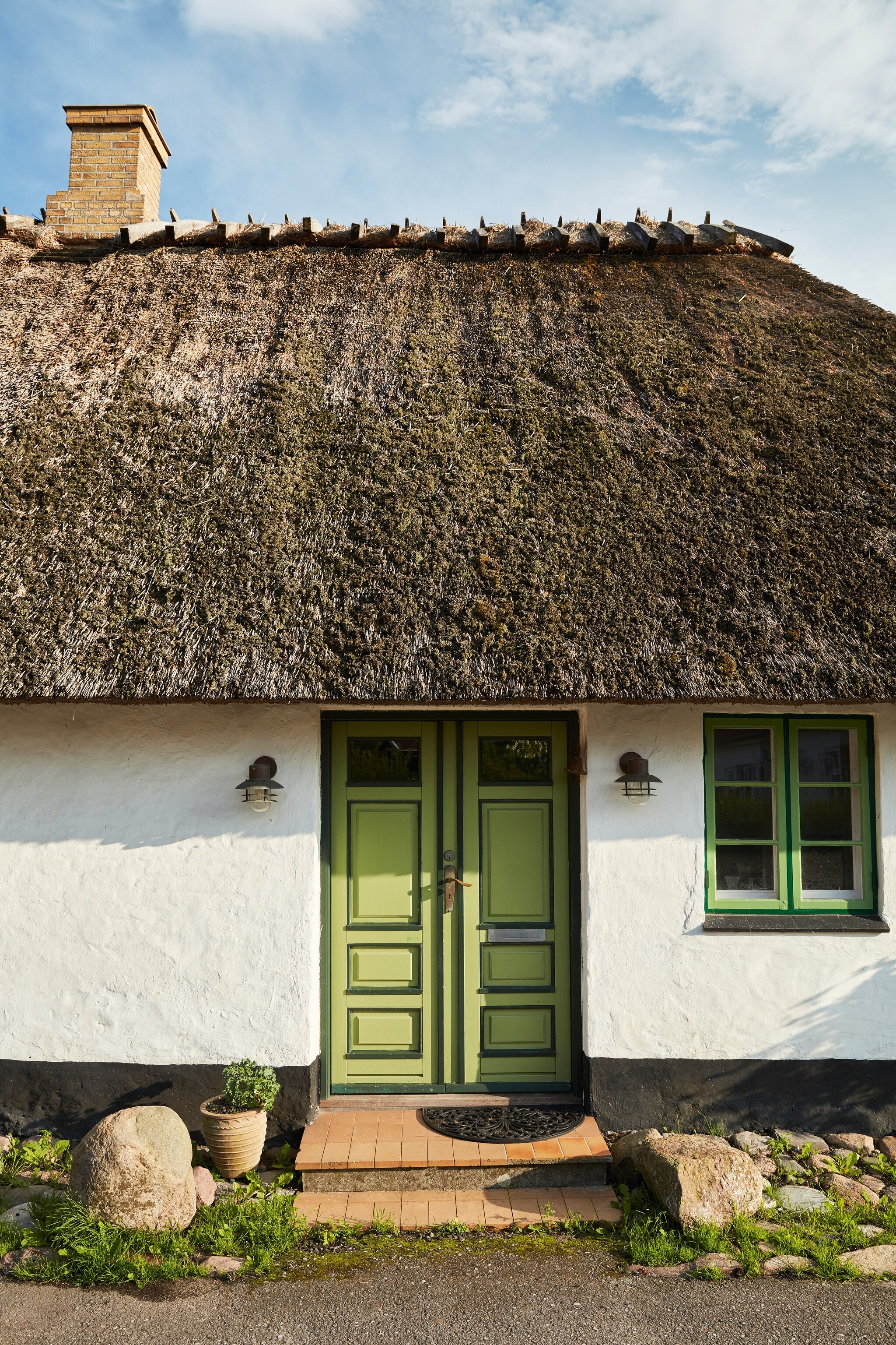 small house painted black, white and green, with brick steps and a thatched roof