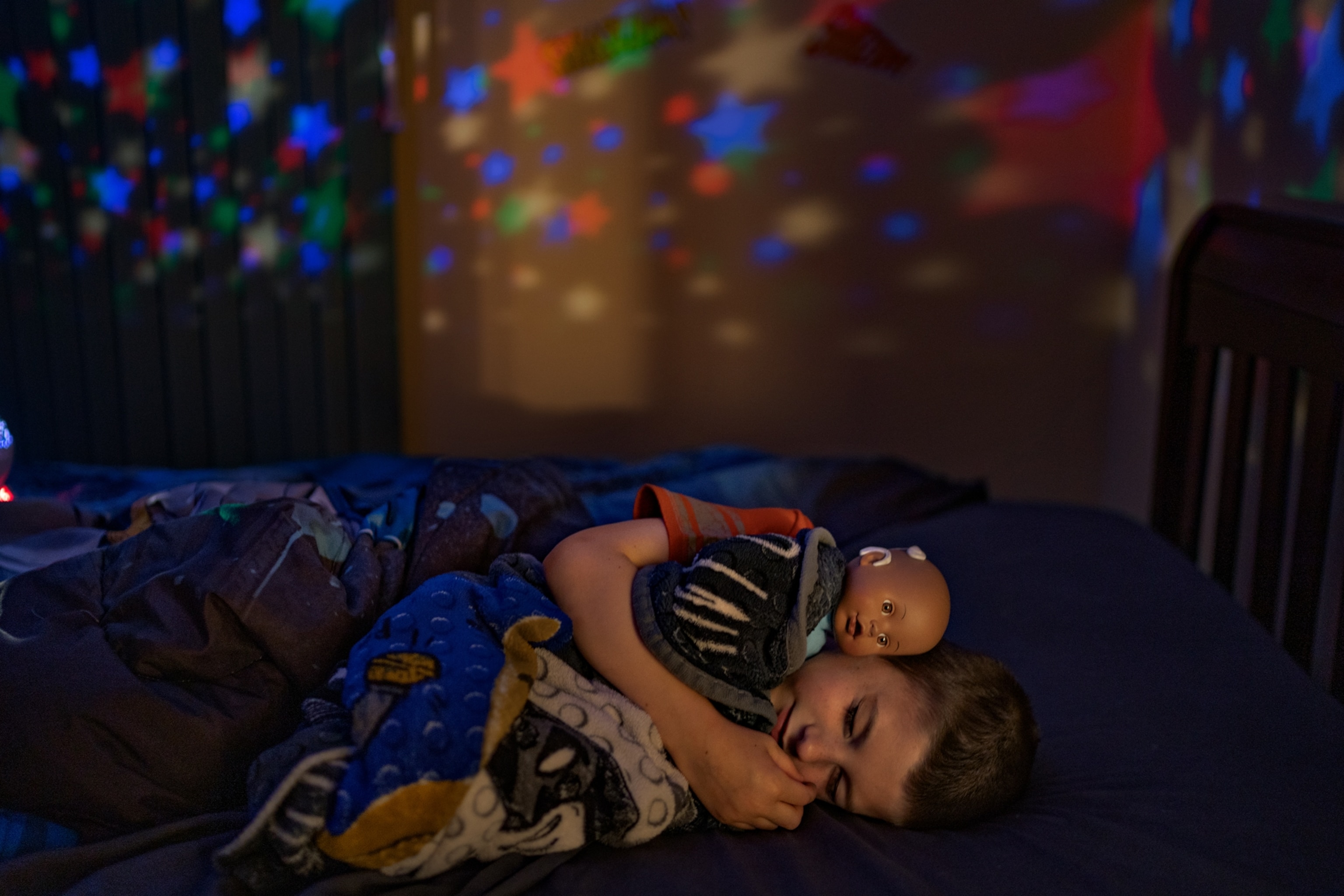 A boy sleeping under star night lights holding a baby doll