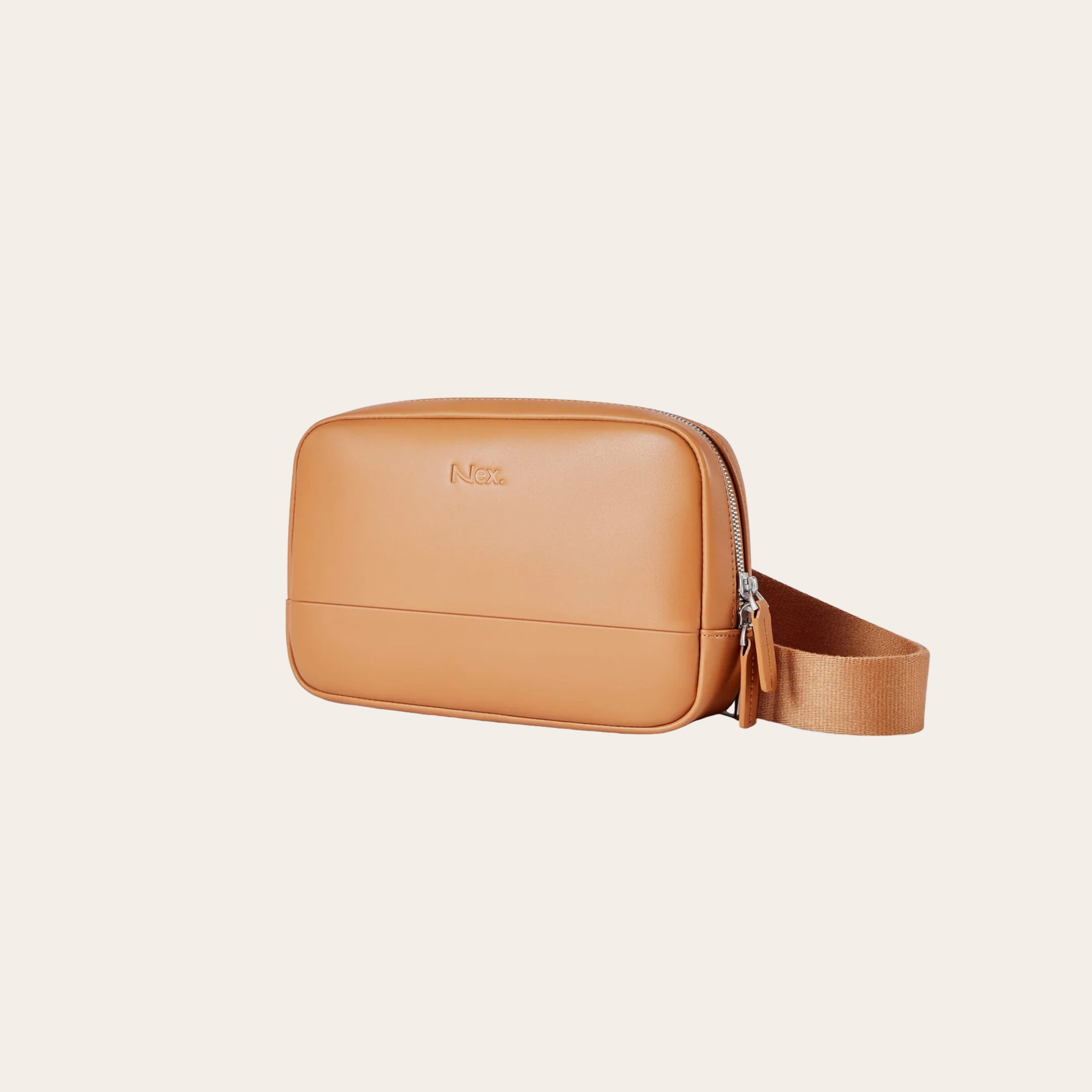 A tan leather bag smooth texture with a fabric strap on a cream background.
