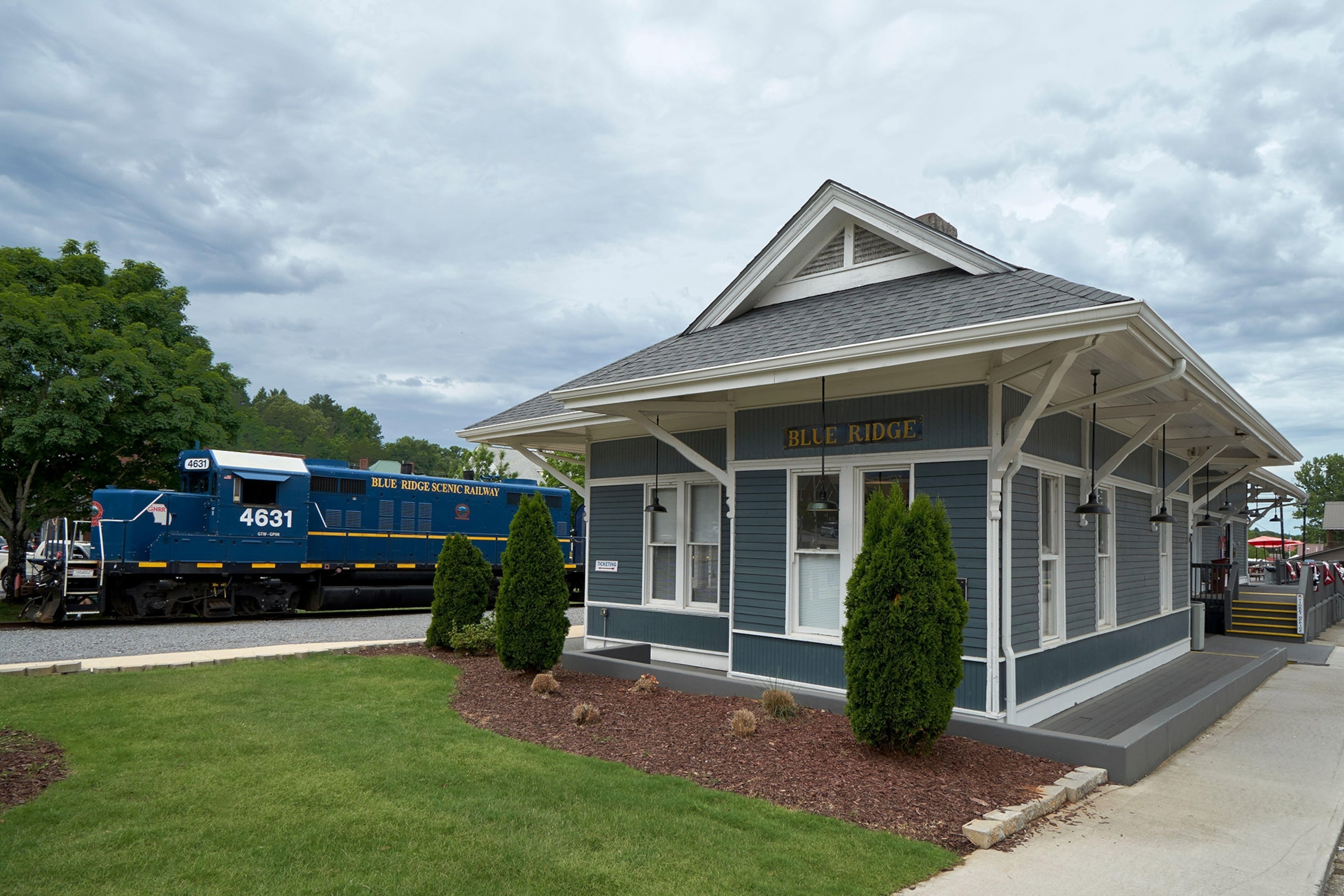 A deep blue train sits idle next to a small building that reads "Blue Ridge" above large windows.