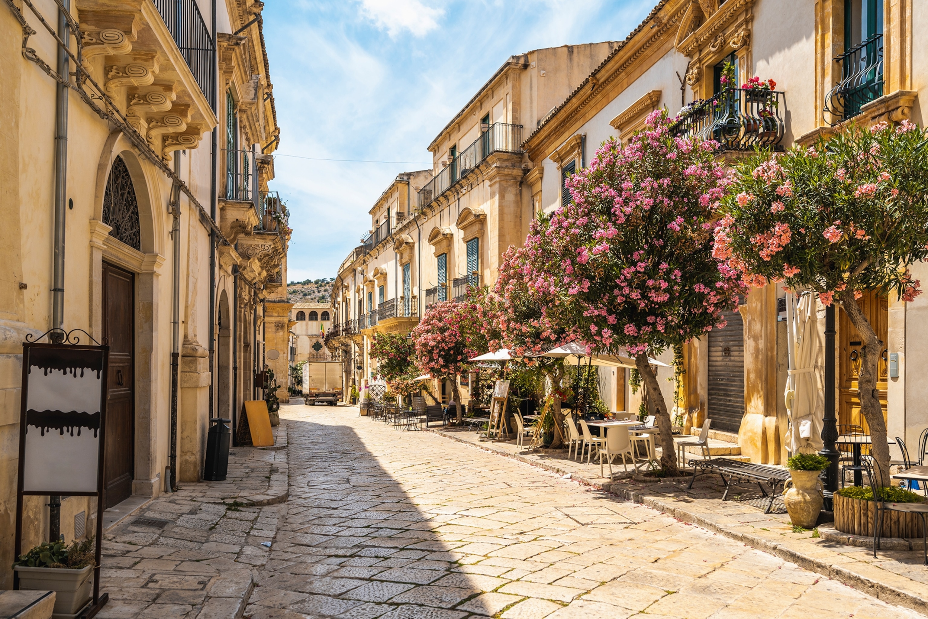Streetview of a cobble-stoned and tree-lined street in the old town of Modica.