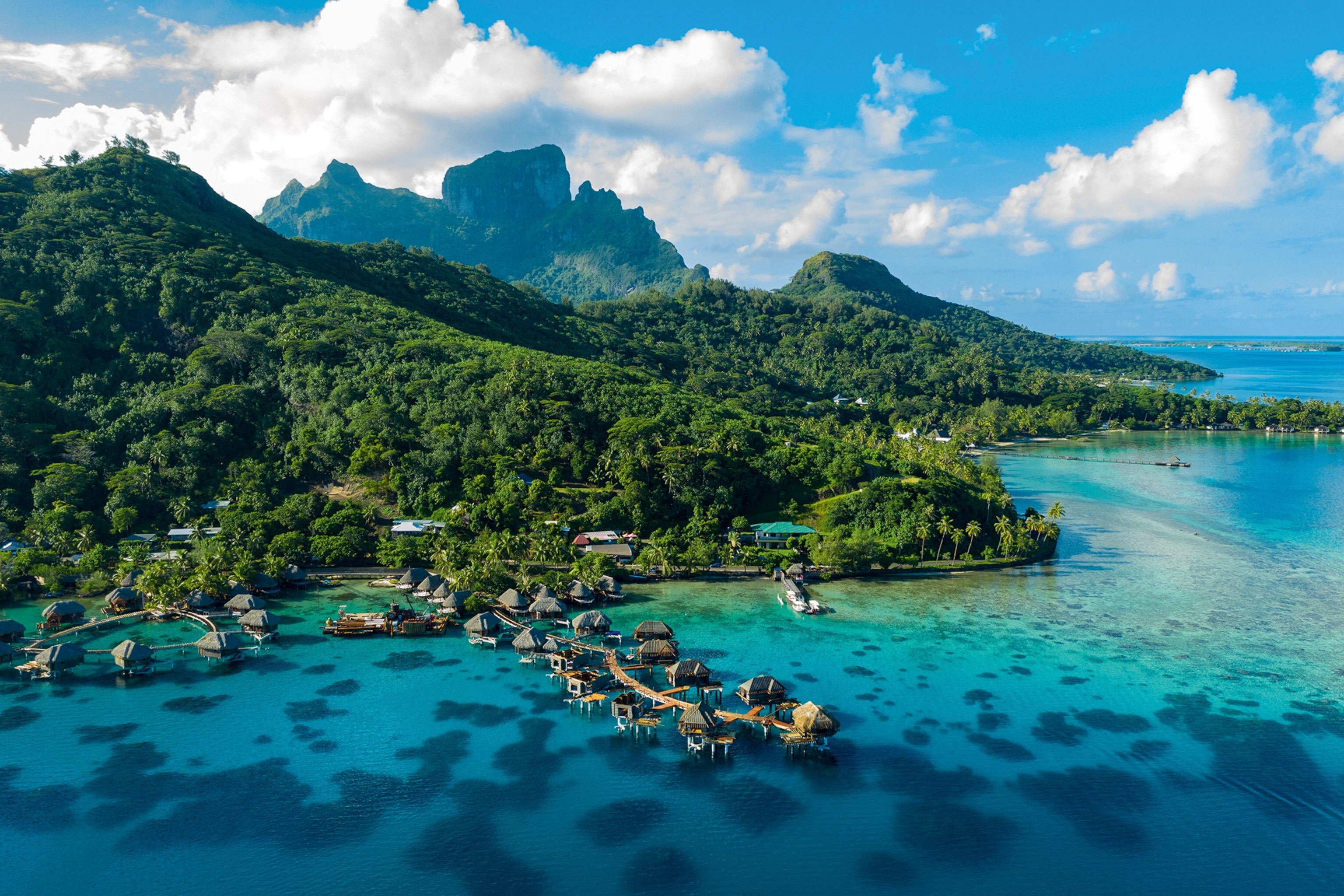 Aerial view of overwater bungalows with a coral reef lagoon and lush vegetation