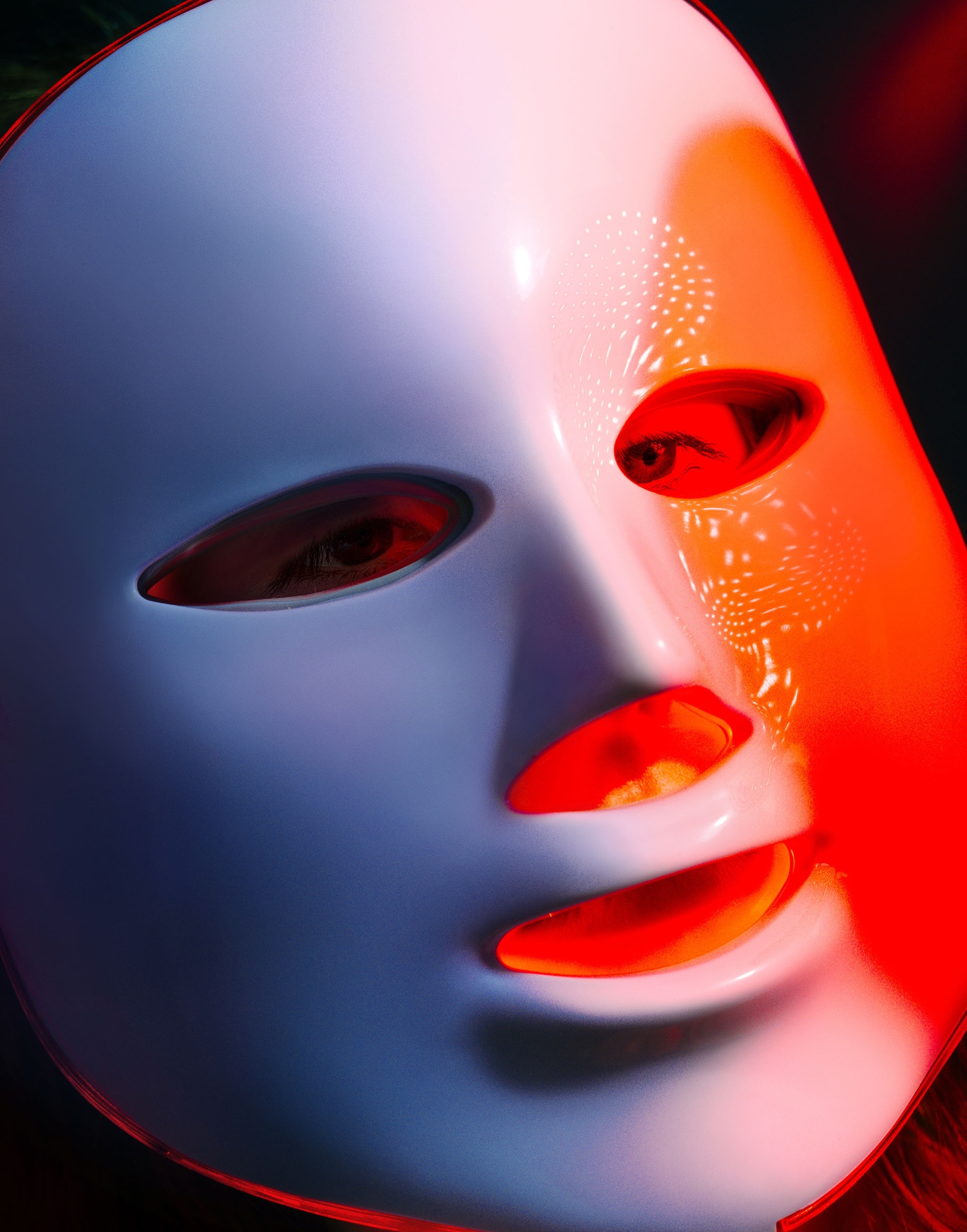 A model poses for a portrait with a red light LED mask designed for consumer use in a studio against a blue background