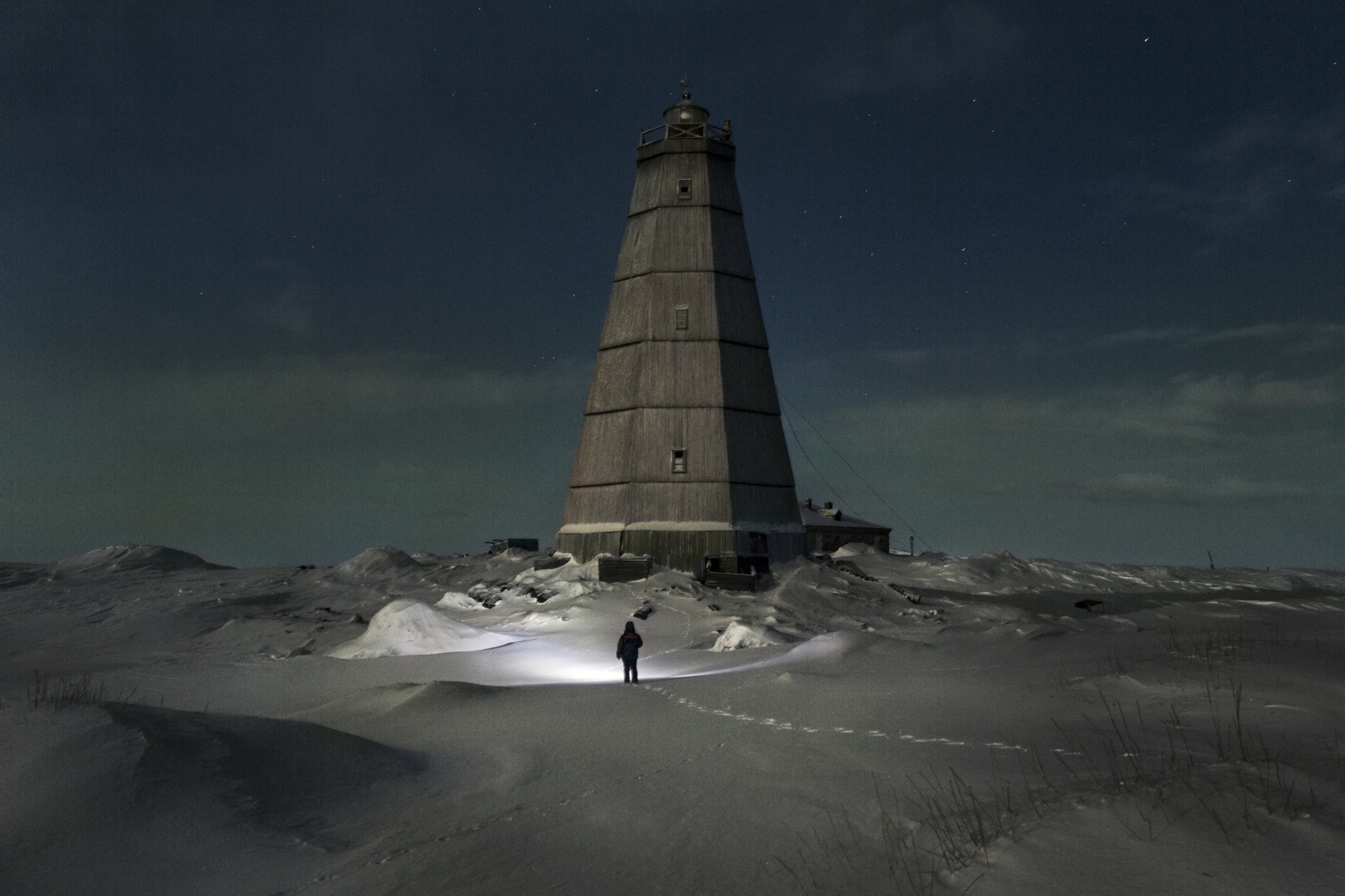 lighthouse at night with human with flashlight near it.