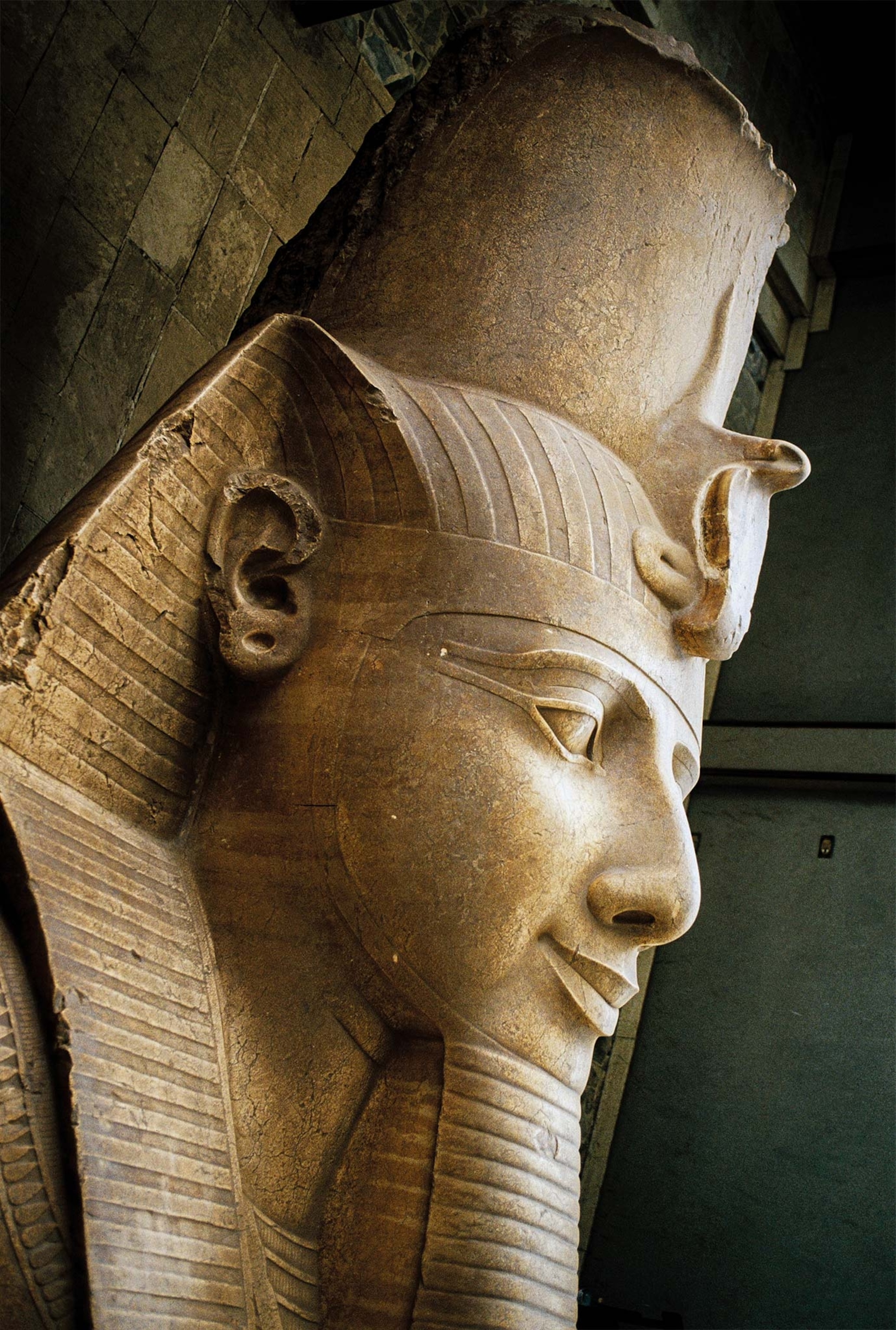 The head of Ramses II’s recumbent colossus at Memphis wears the nemes, or striped head cloth, and the royal uraeus serpent of divinity and authority.