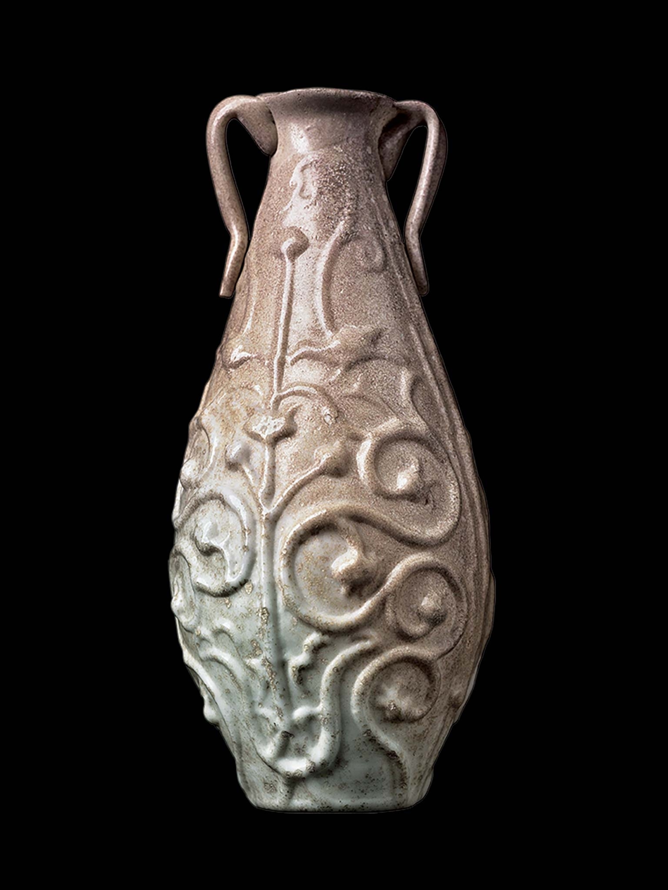 A thin-necked bottle make of mold-blown glass with floral scrolls and floating handles stands at four inches
