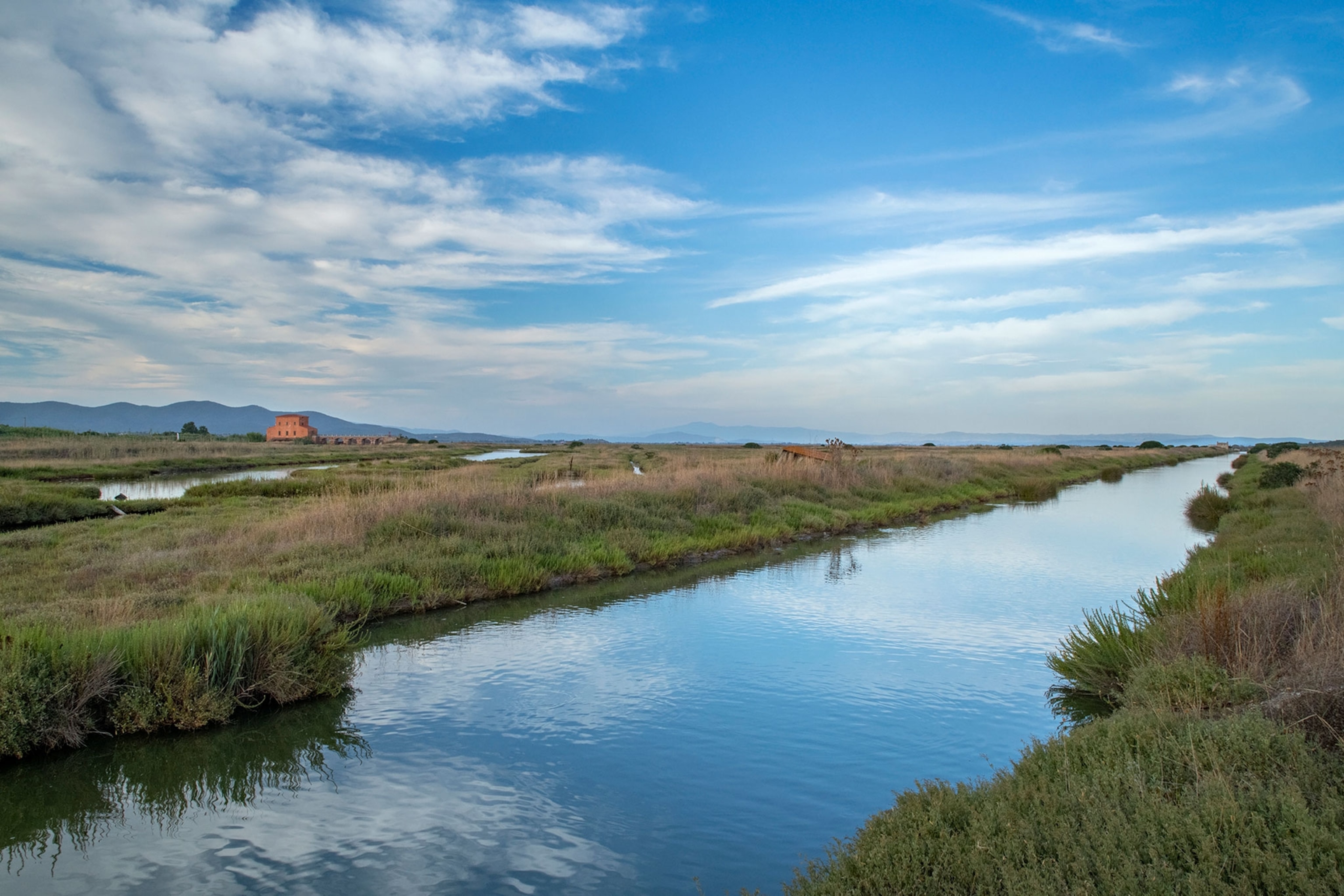 A small red building stands in the distance amongst a vast marshland.