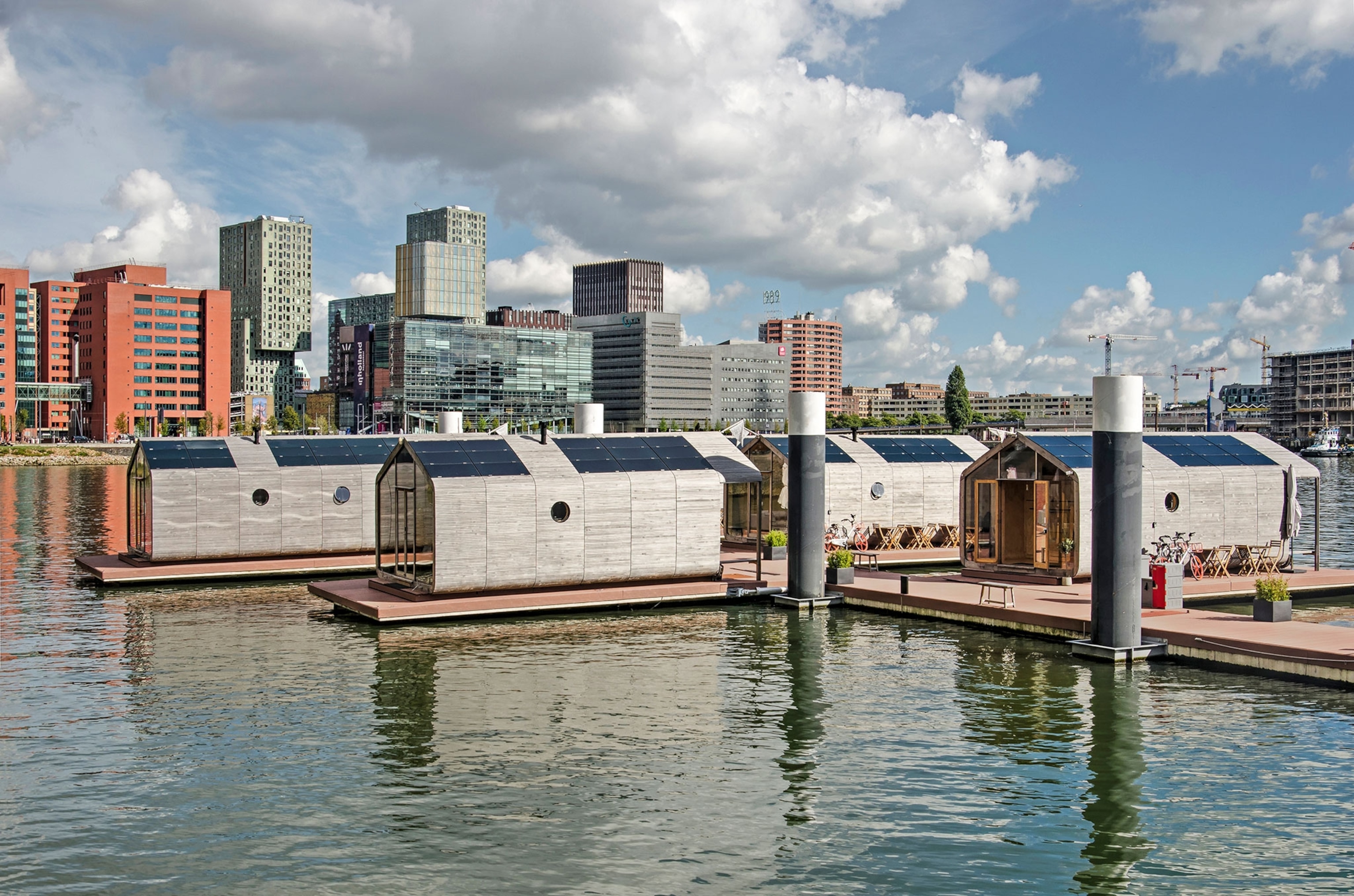 A row of small, grey homes with solar panels floating on the water.