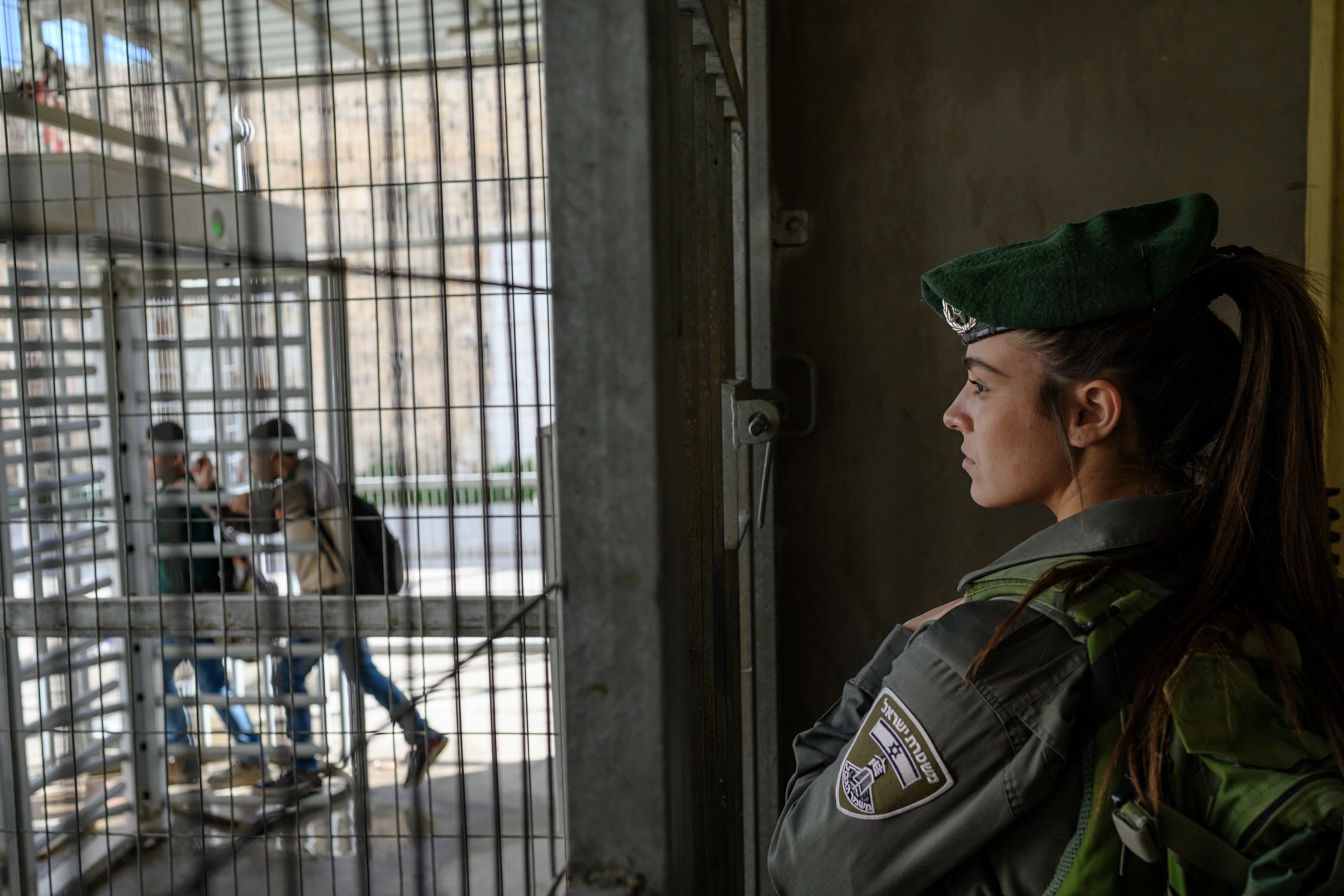 a policewoman gazing out of metal fence at a checkpoint