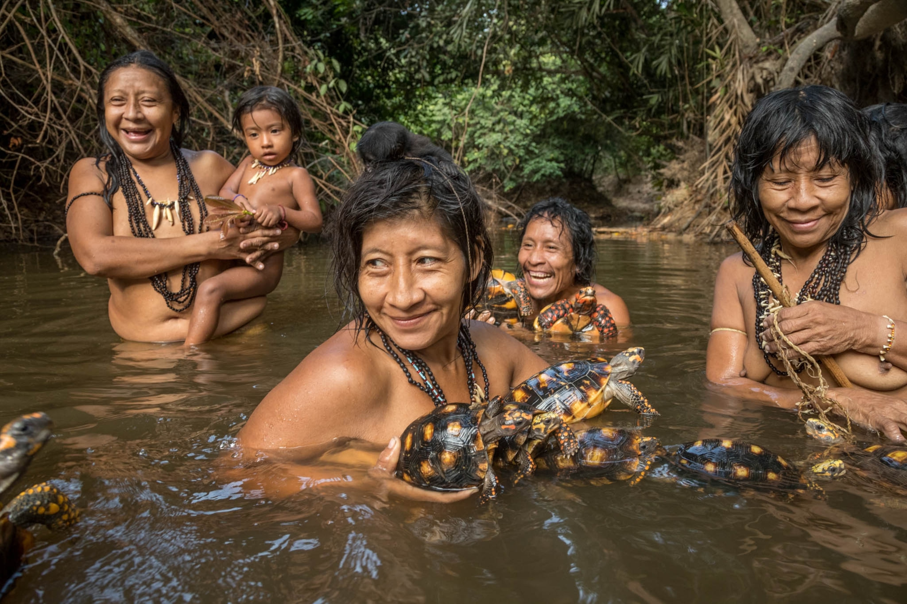 women, and a man, and a young child smiling and holding tortoises in a river