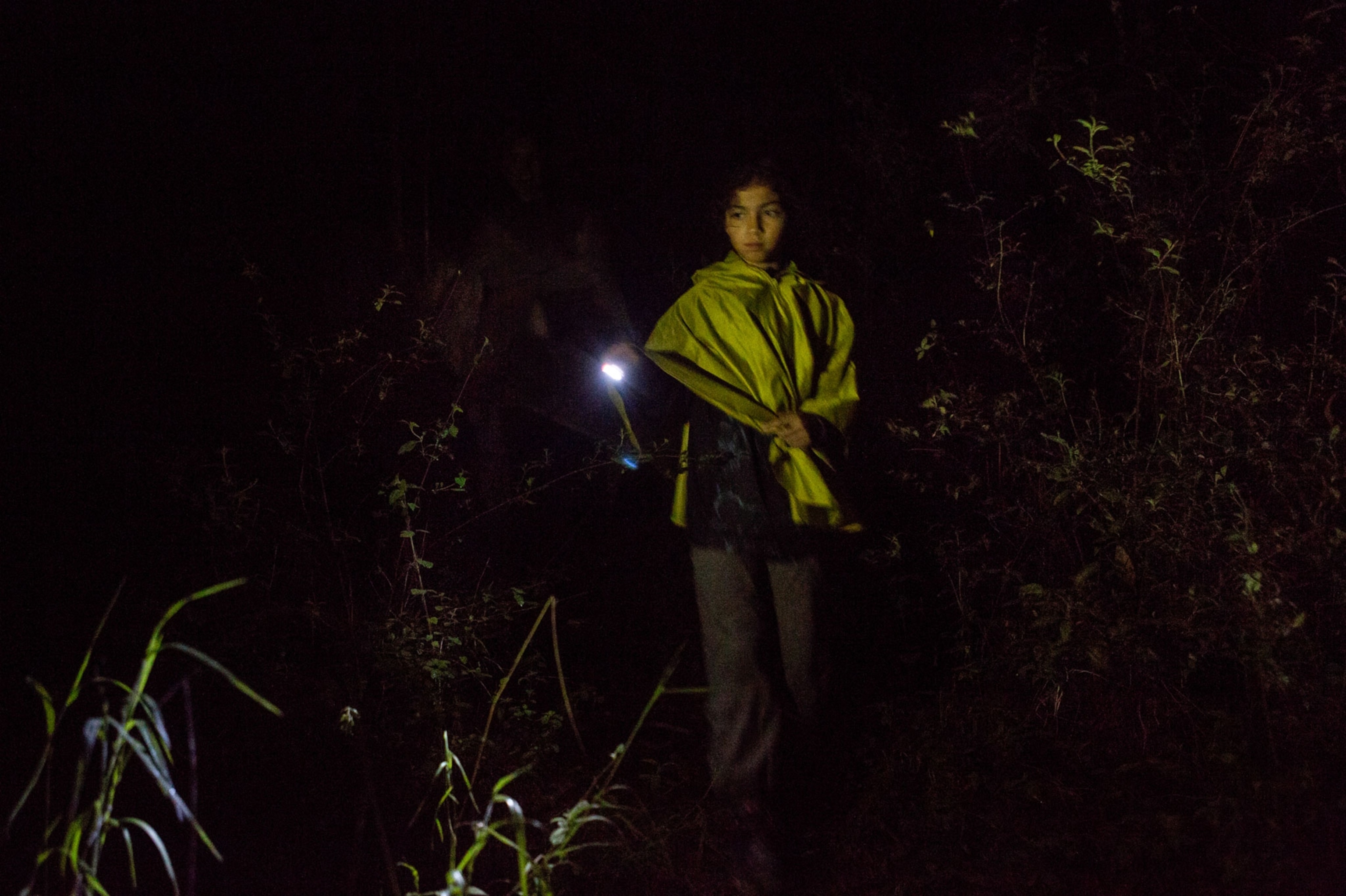 a girl walking through the woods with a flashlight