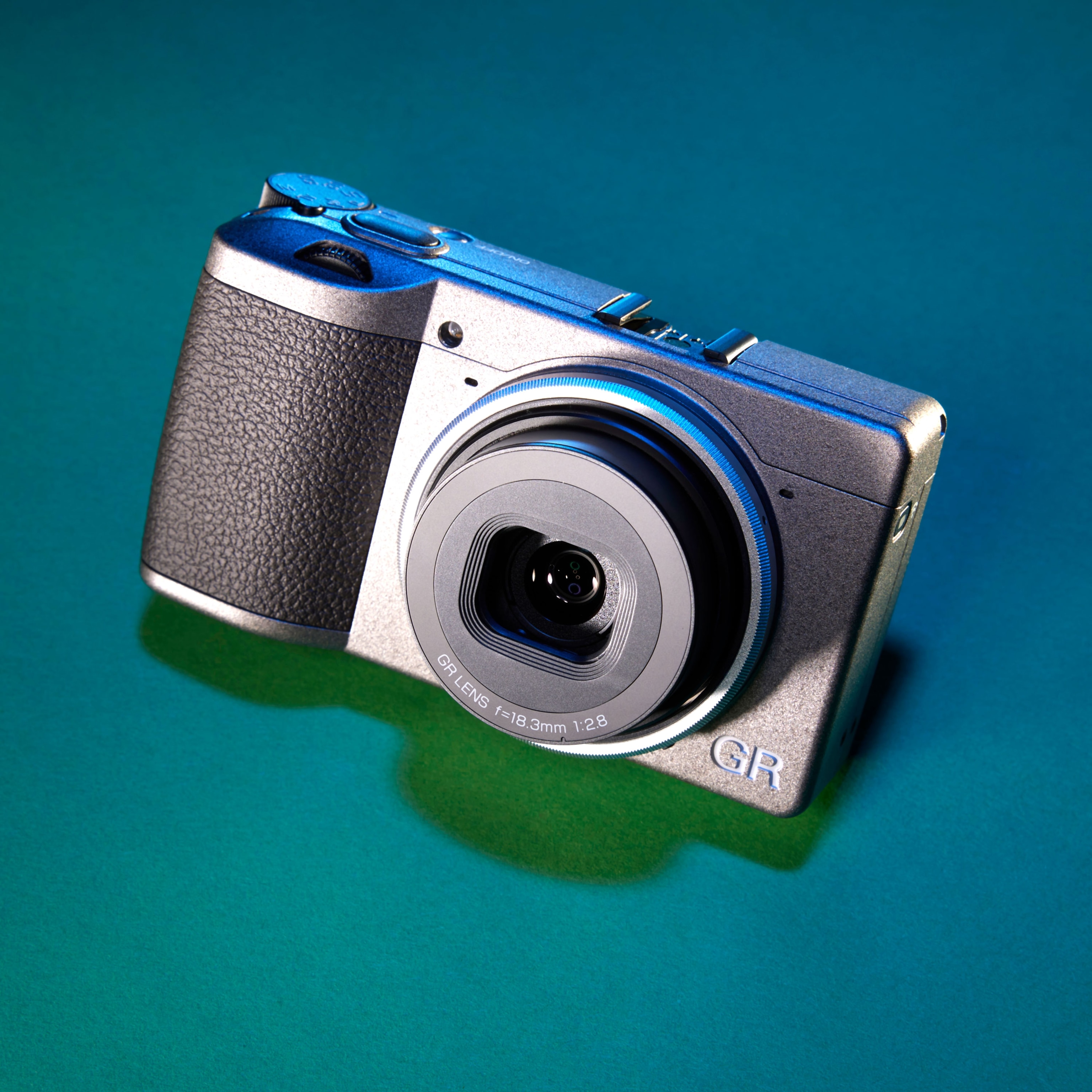 Studio photograph of the Ricoh GRIII camera against a teal gradient background