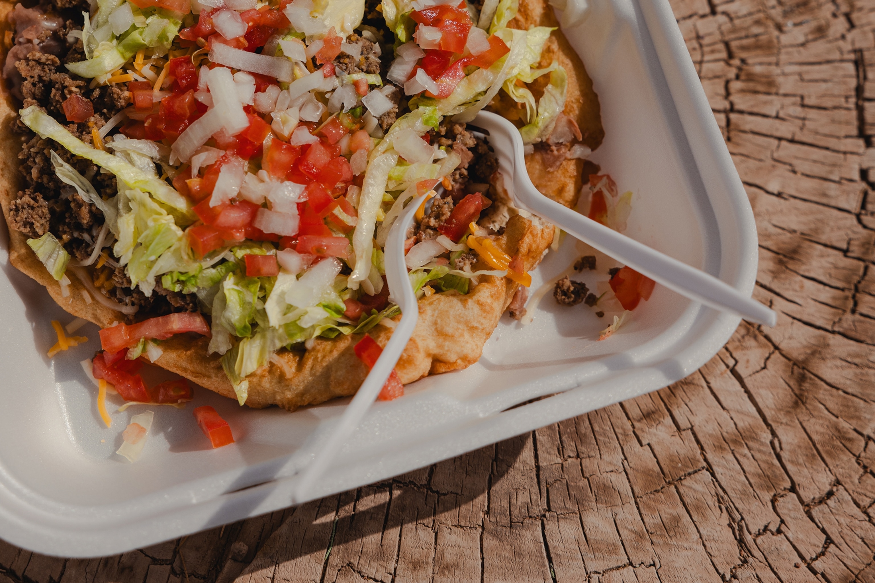 A close up shot of a taco in a white poly container. The taco is topped with pico de gallo.