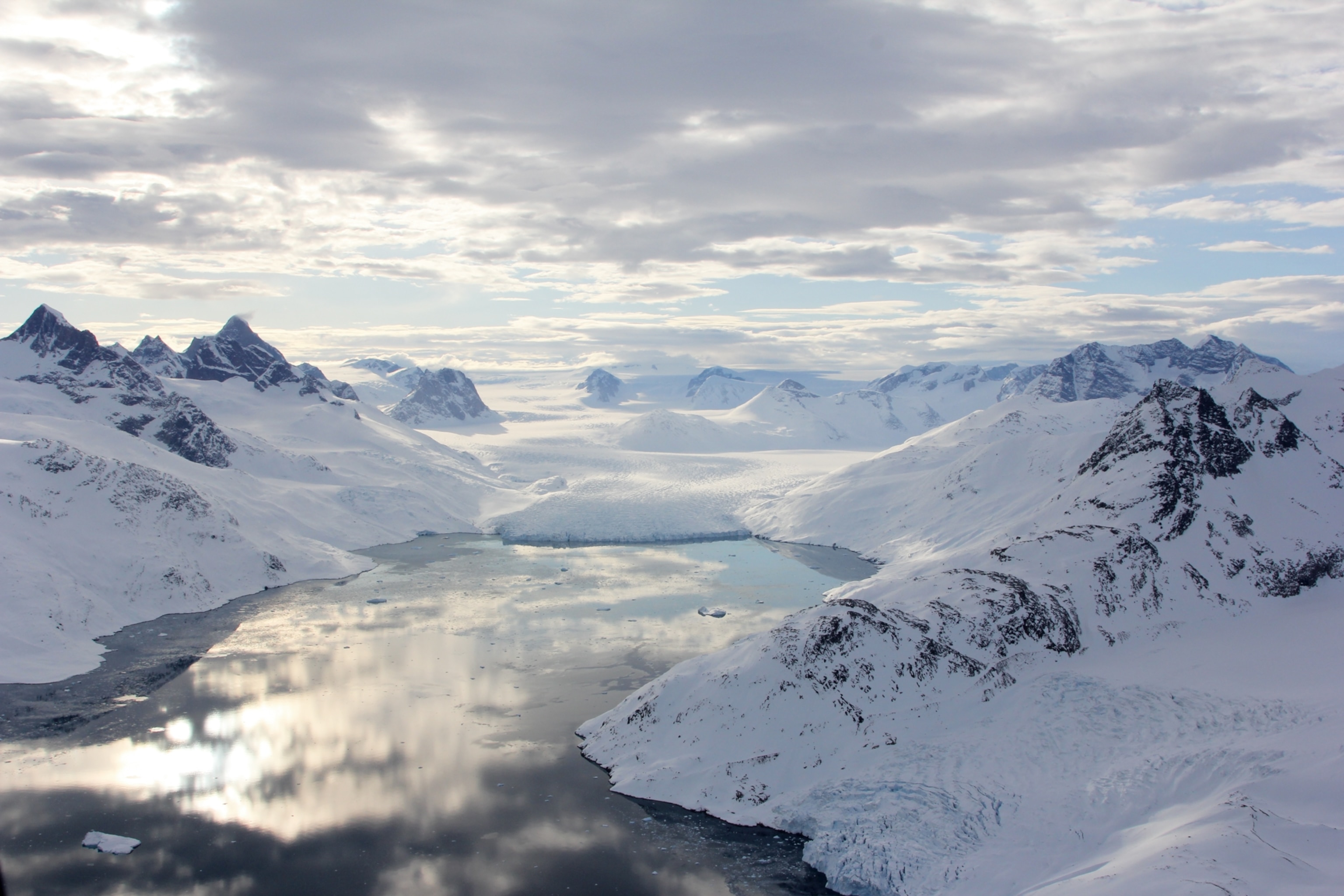 Picture of a fjord surrounded by snow covered mountains.