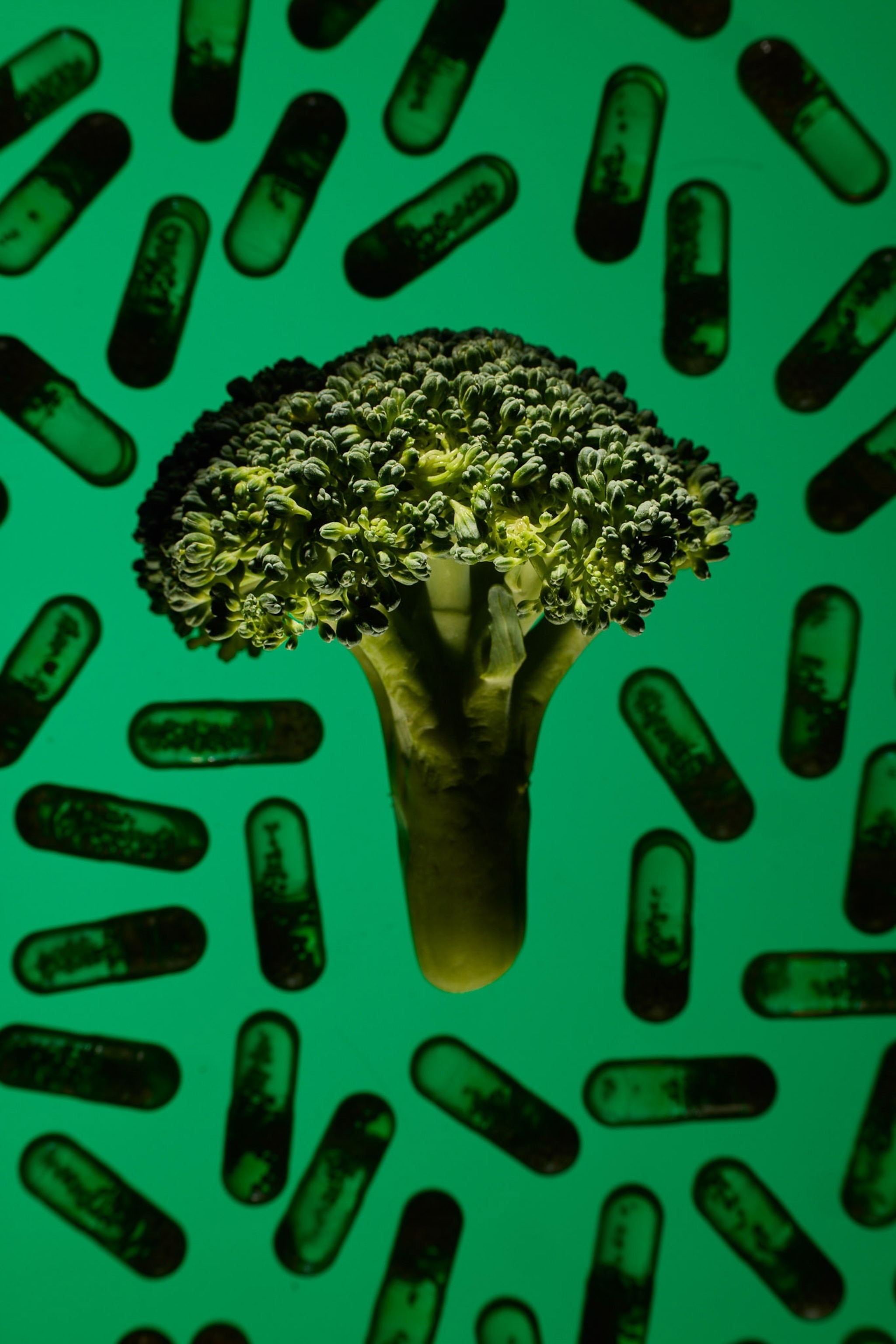 Brocolli is higlighted on a flat lay with light on a green background with sillouheted multi vitamins.