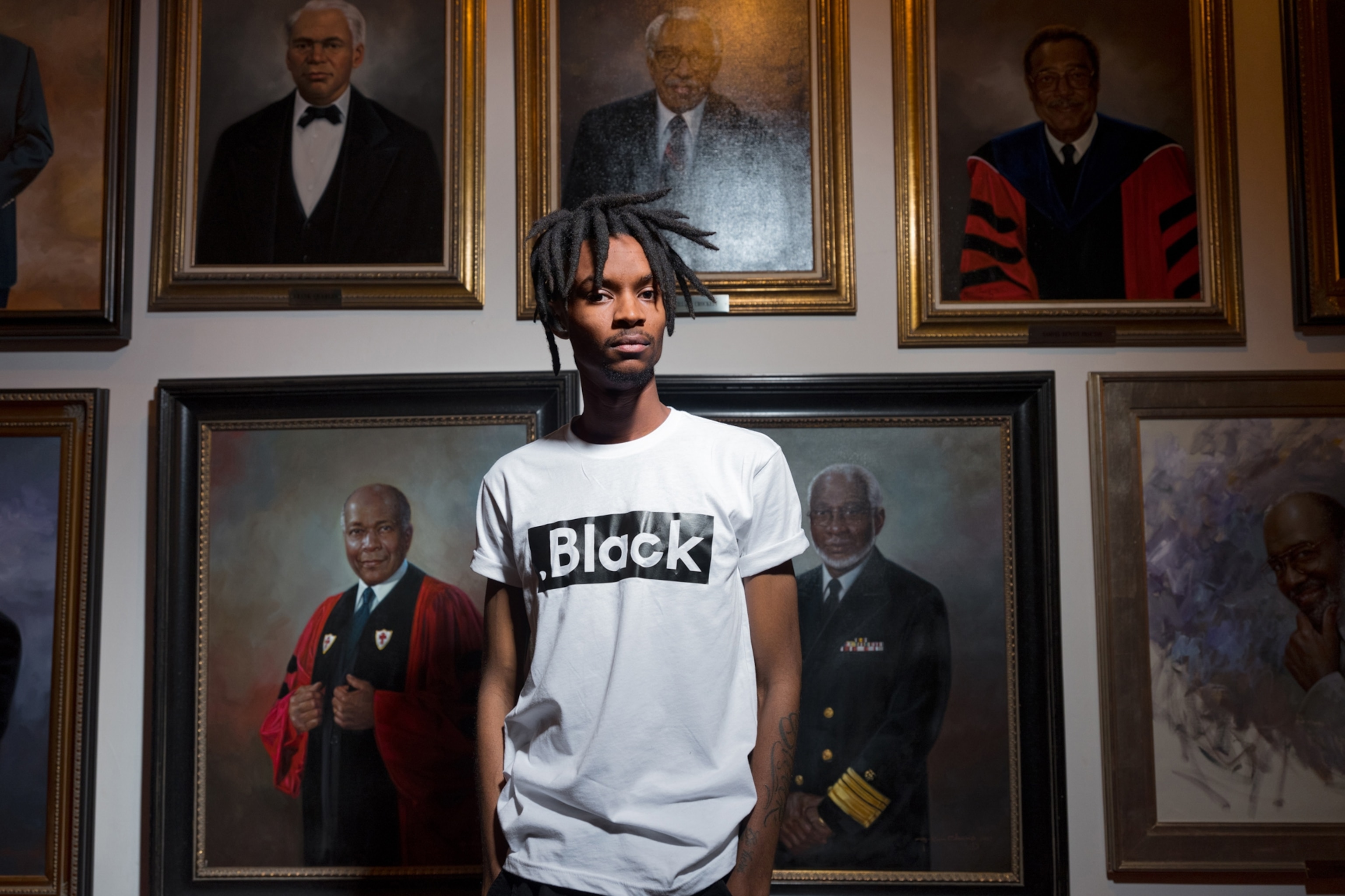 young black man standing for a portrait wearing a white t-shirt that says "black"
