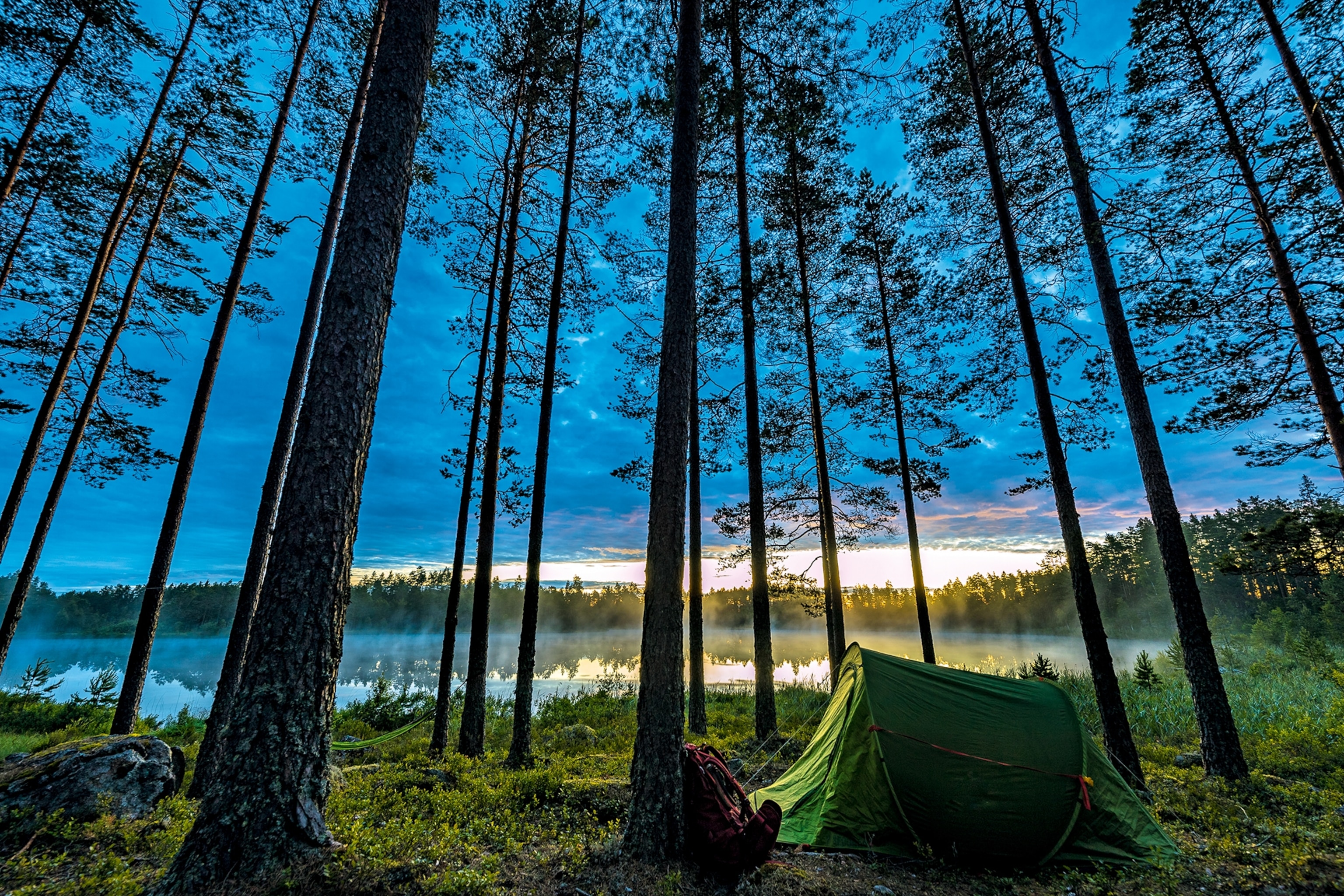 A green tent set up by a lake at nigthfall
