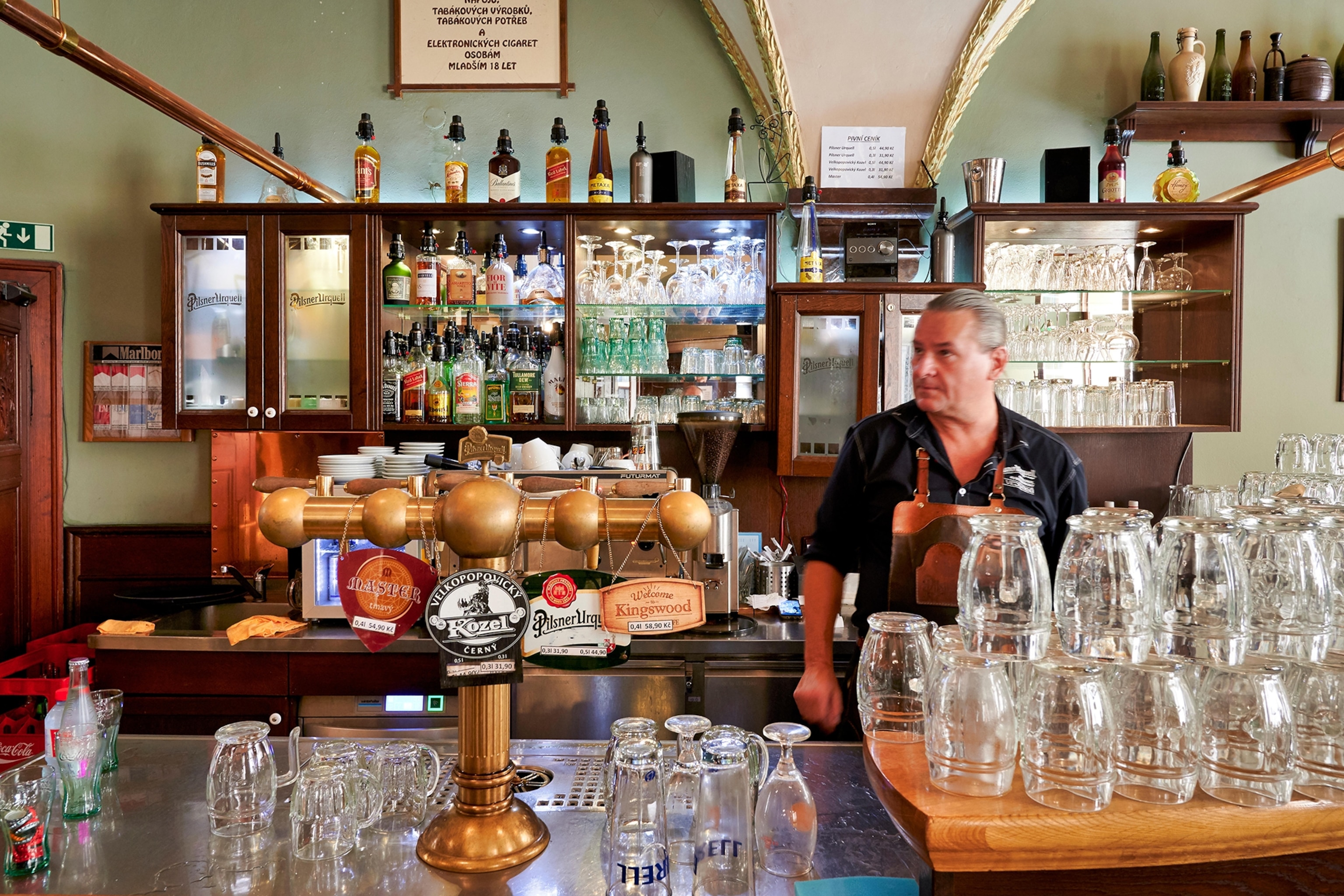 Man stands behind a bar lined with glasses, bottles and beer pumps
