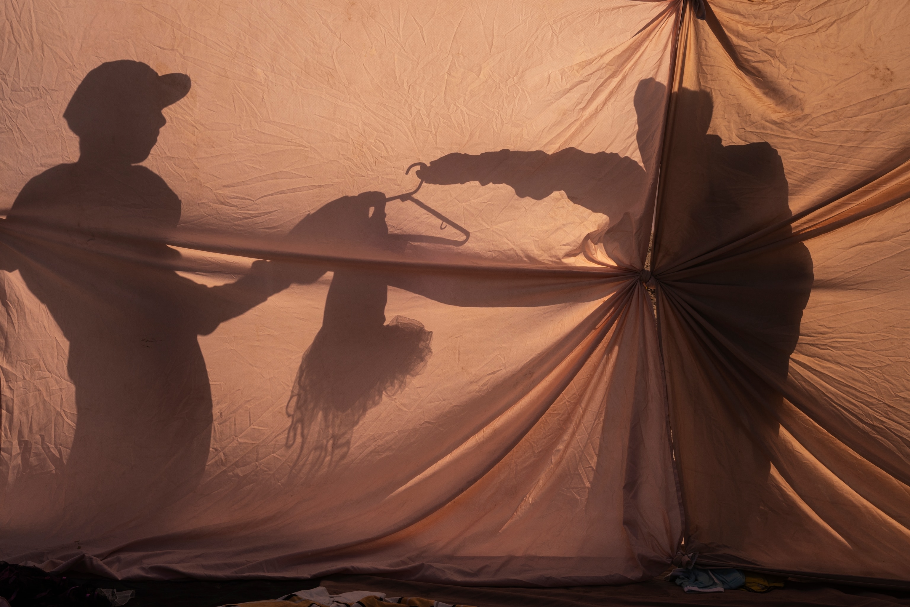shadows of two individuals who are standing in front of a sheet holding up clothing.