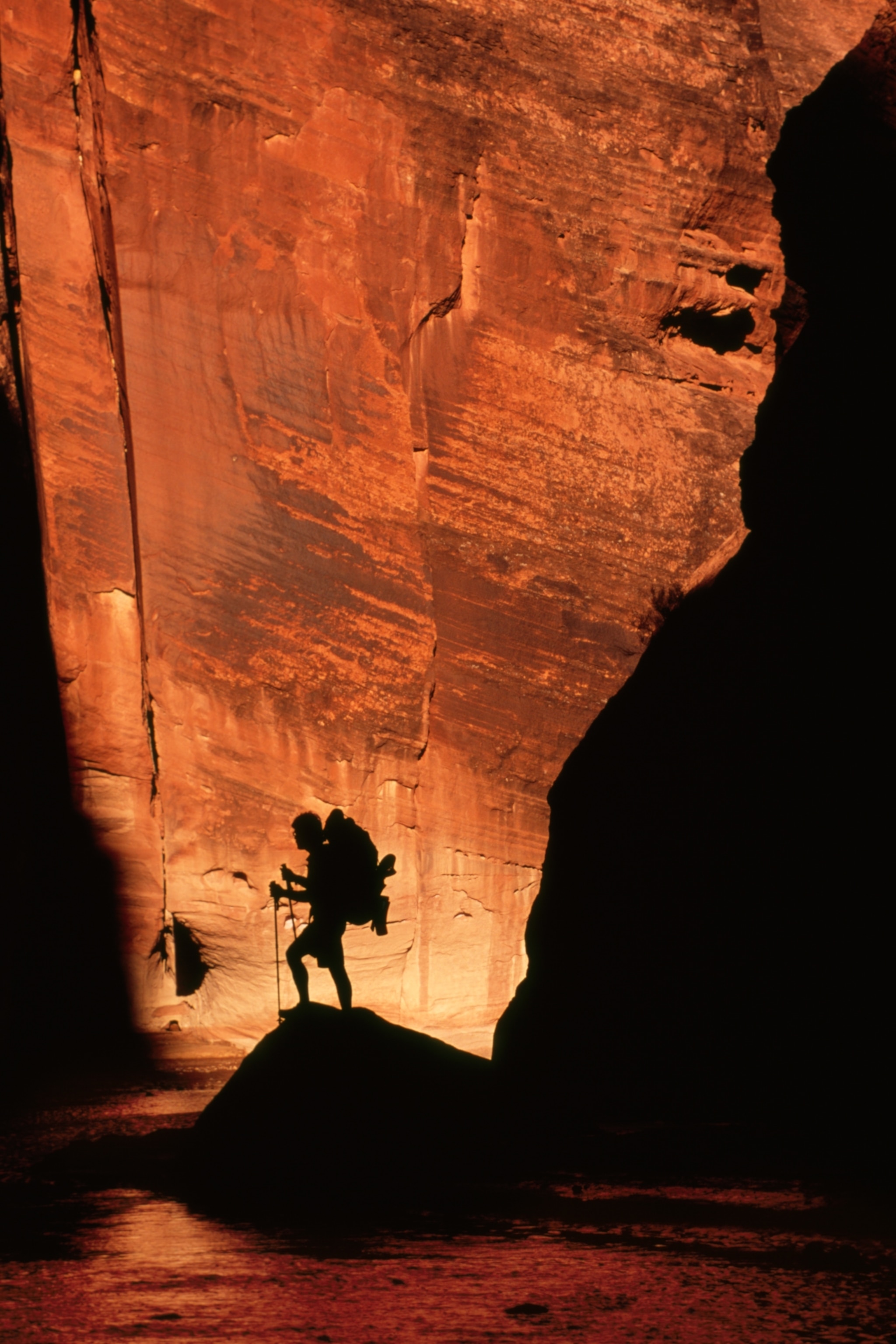 A hiker silhouetted against the orange walls of a slot canyon.