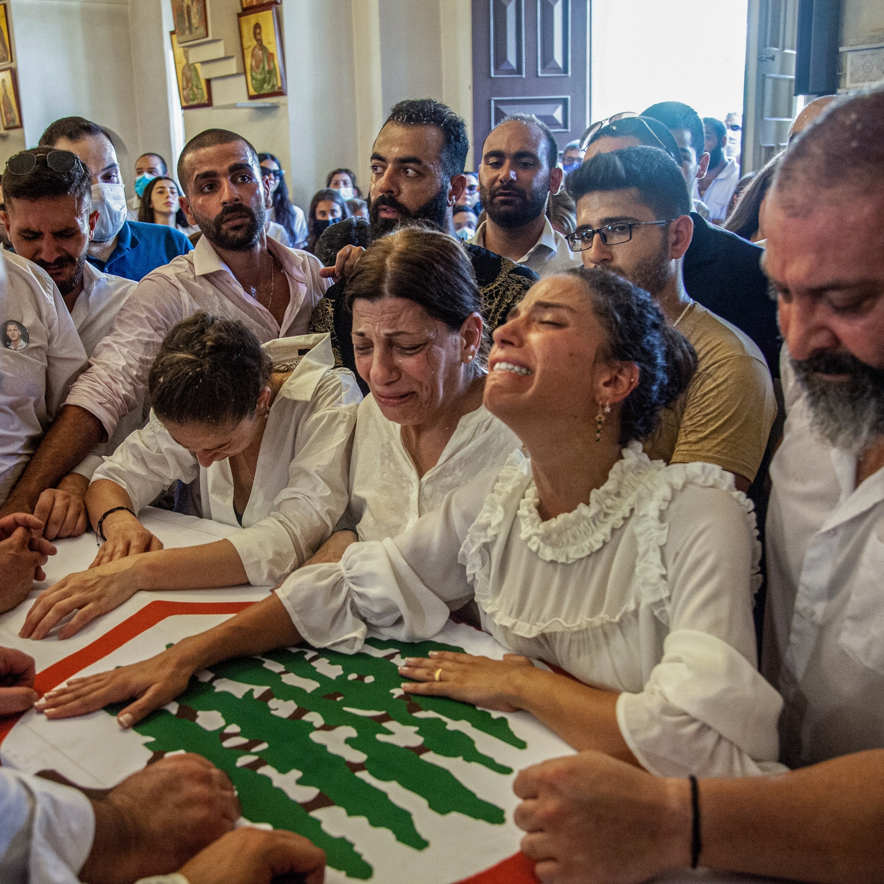 Picture of a group of people all wearing white carrying a casket with multiple women and men sobbing.