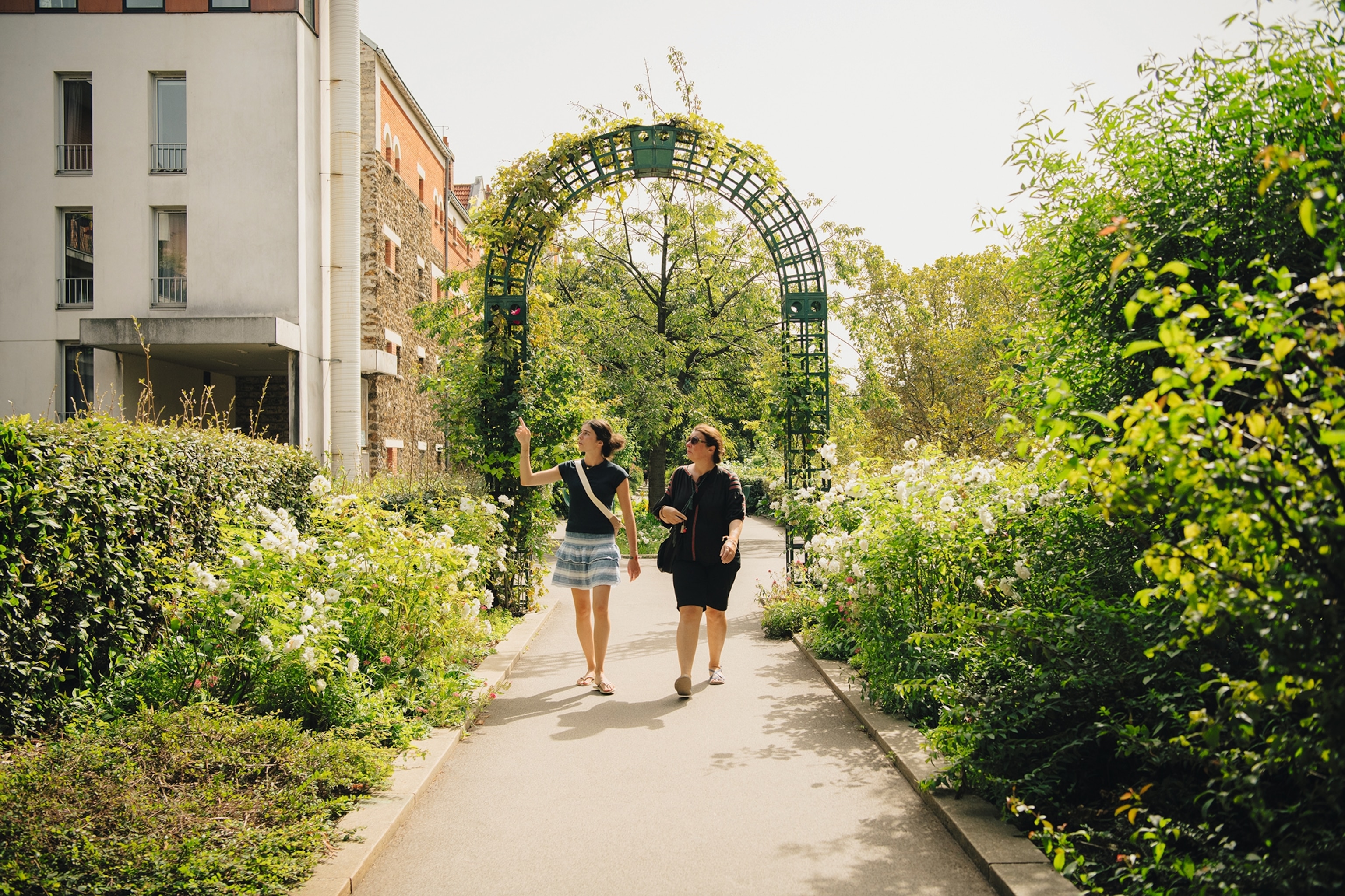 Two people walking through the vy-covered arches on the Coulée Verte - a rail road which circles Paris.