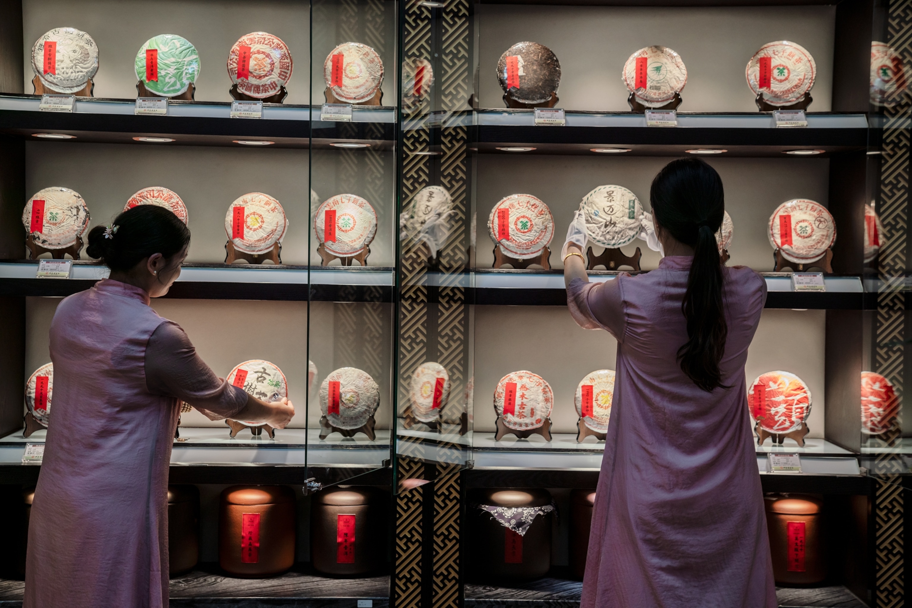 Two women tend to packaged tea cakes in a display case of numerous prized tea cakes.