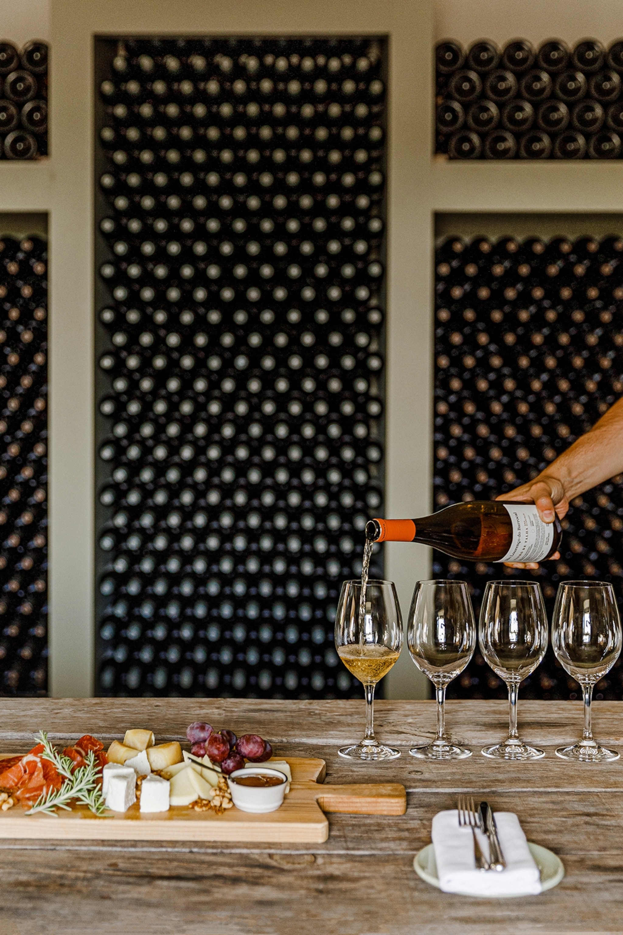 A cheeseboard is resting to the side of a line of glasses, being filled with wine.