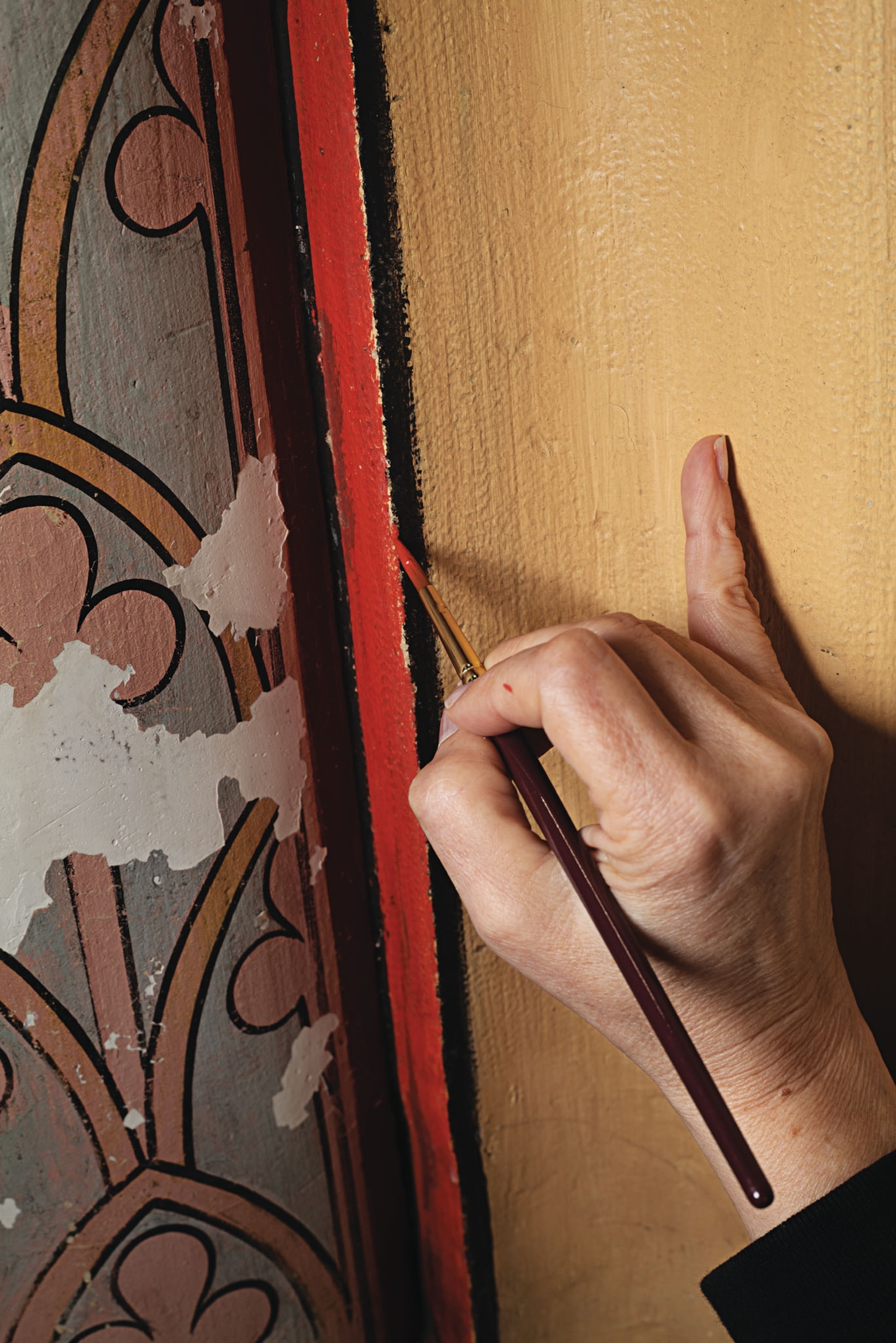 A person is carefully restoring the wall, paint red paint with a small brush and precision.