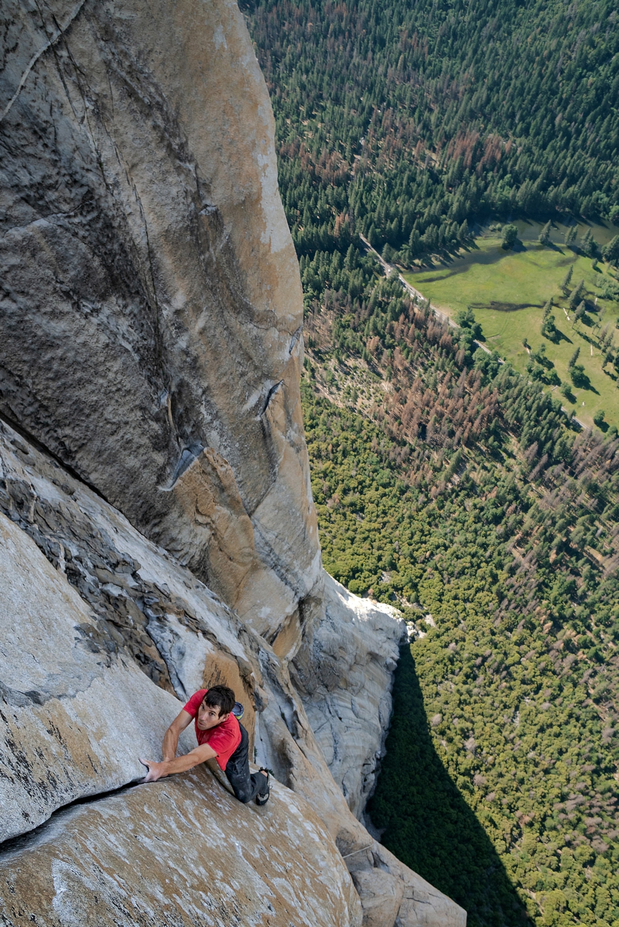 man in red shirt on the vertical wall without ropes high above ground