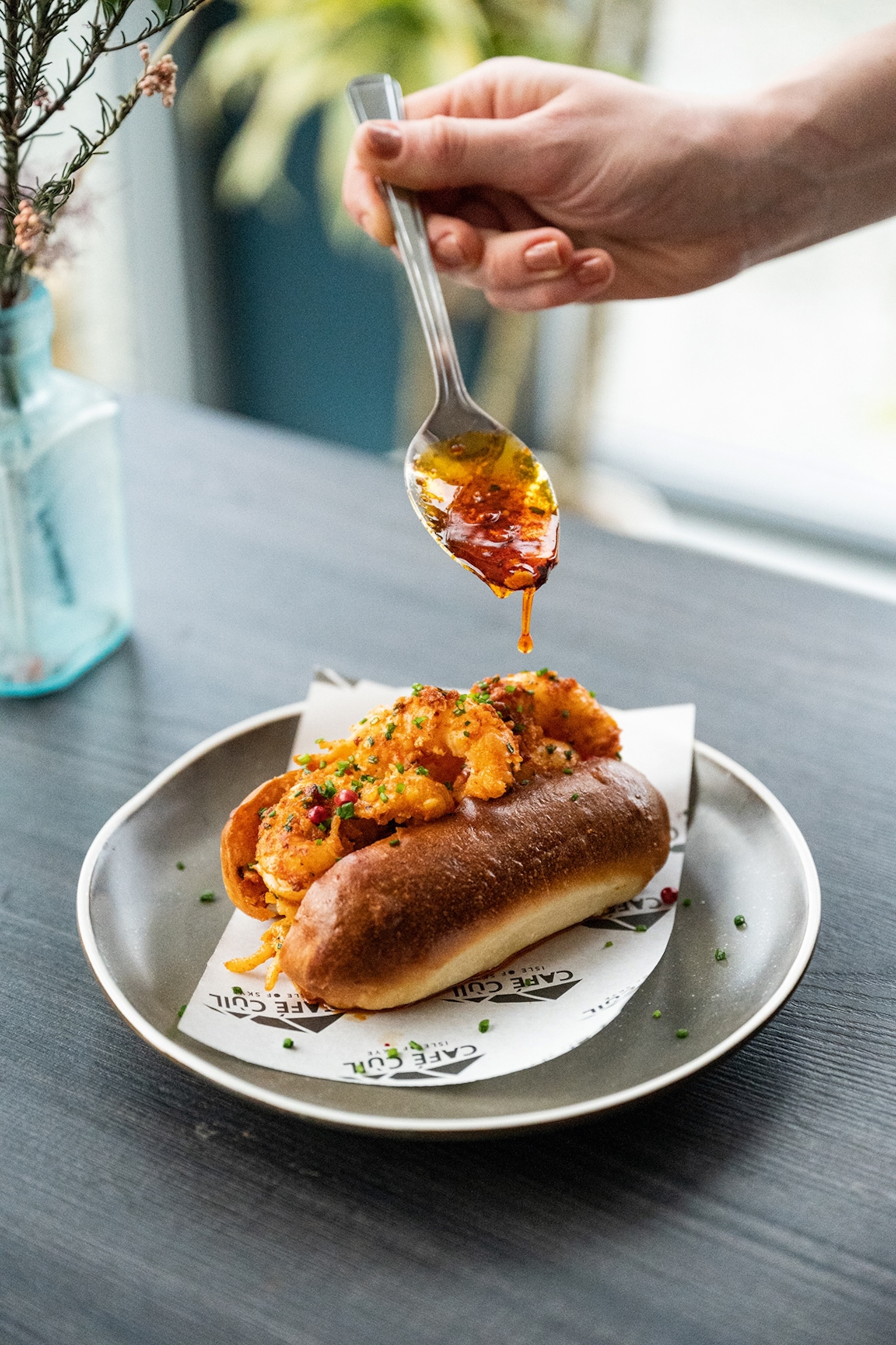 Spoon held over an egg roll with red sauce dripping onto the food
